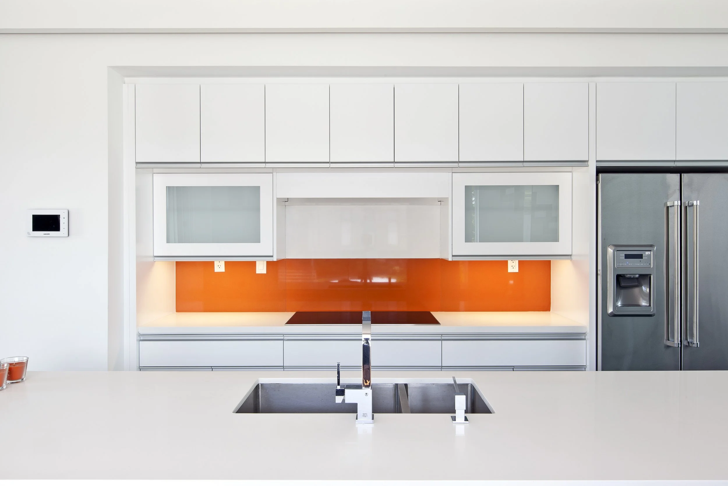 Patio House kitchen in North York, Toronto, built by Maxamin Homes, with white cabinets, orange backsplash, stainless refrigerator, and island sink.