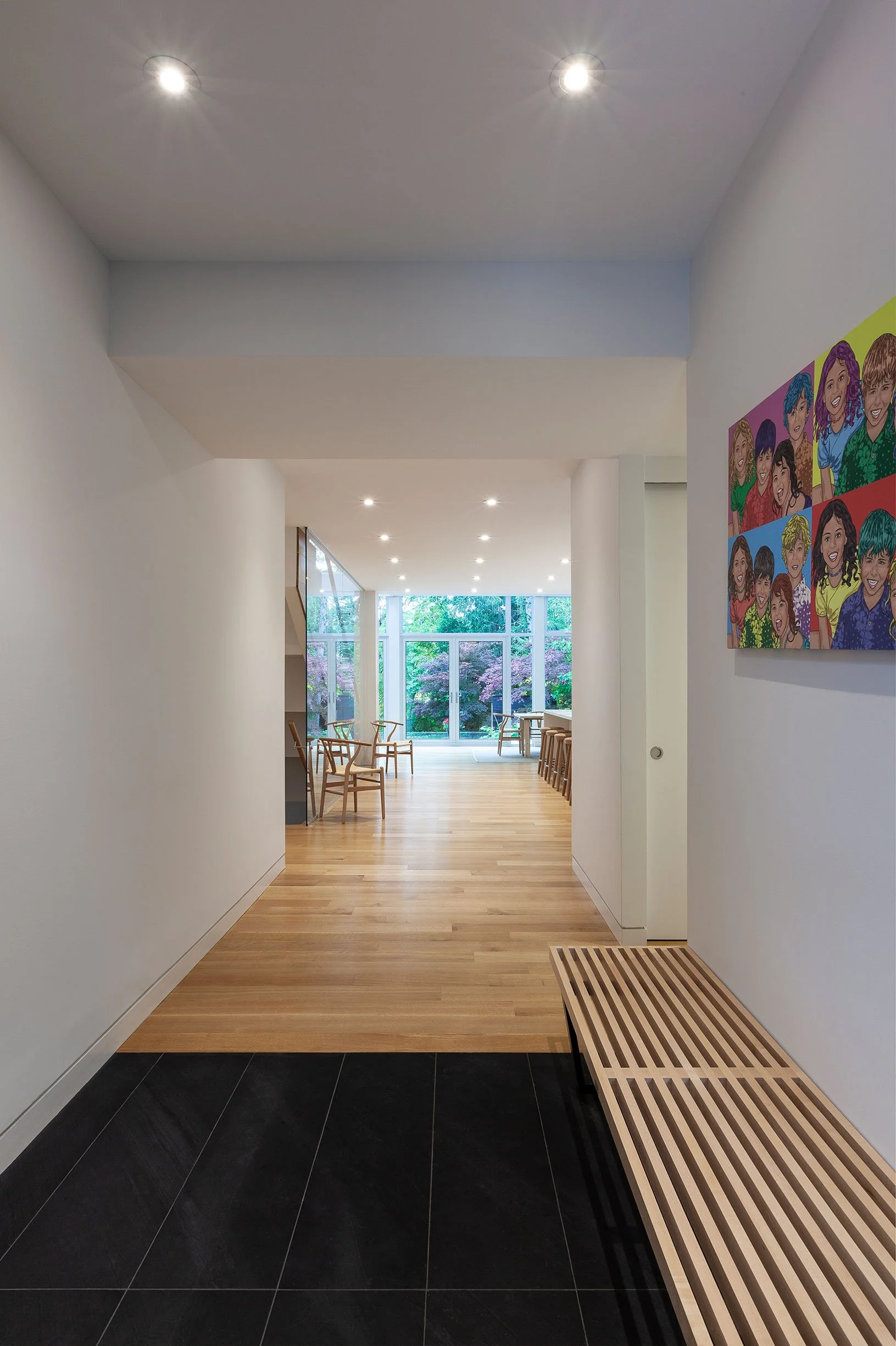 Fun House interior hallway in East York, Toronto, built by Maxamin Homes, with wood floors, white walls, colorful artwork, and garden view through glass doors.