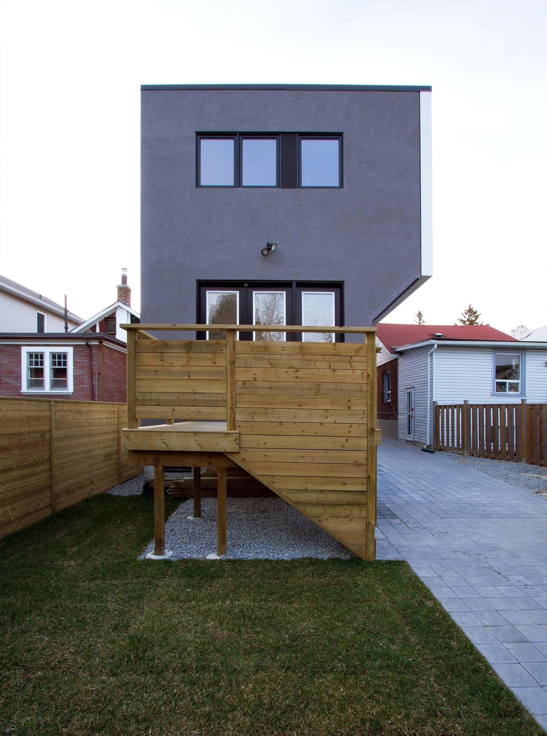 Whale House rear view in East York, Toronto, built by Maxamin Homes, gray multi-story design with balcony, wood stairs, and fenced yard.