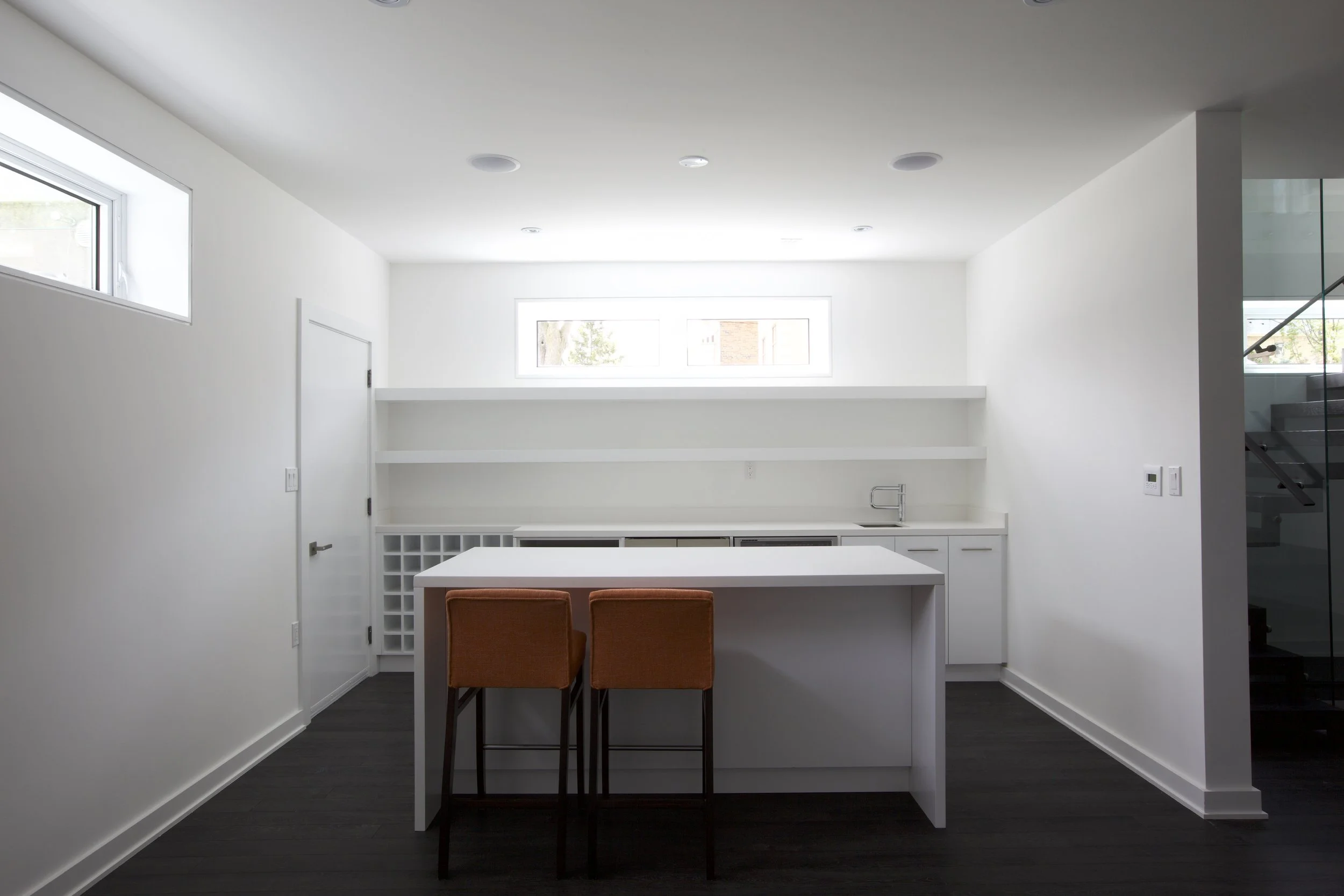 Patio House kitchen in North York, Toronto, built by Maxamin Homes, with small island, orange stools, high window, and dark wood flooring.