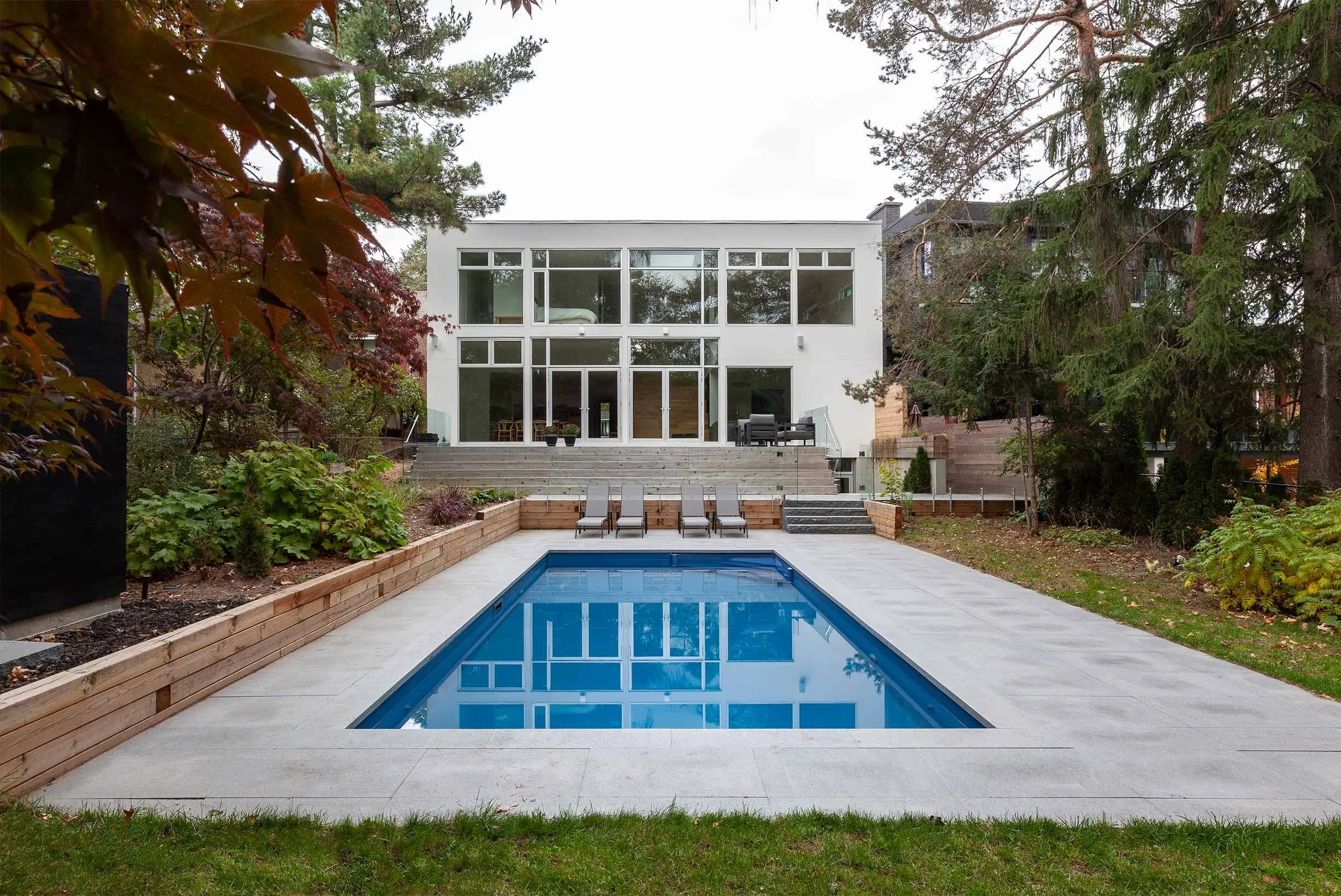 Fun House exterior in East York, Toronto, built by Maxamin Homes, with large glass windows overlooking pool area surrounded by greenery and trees.