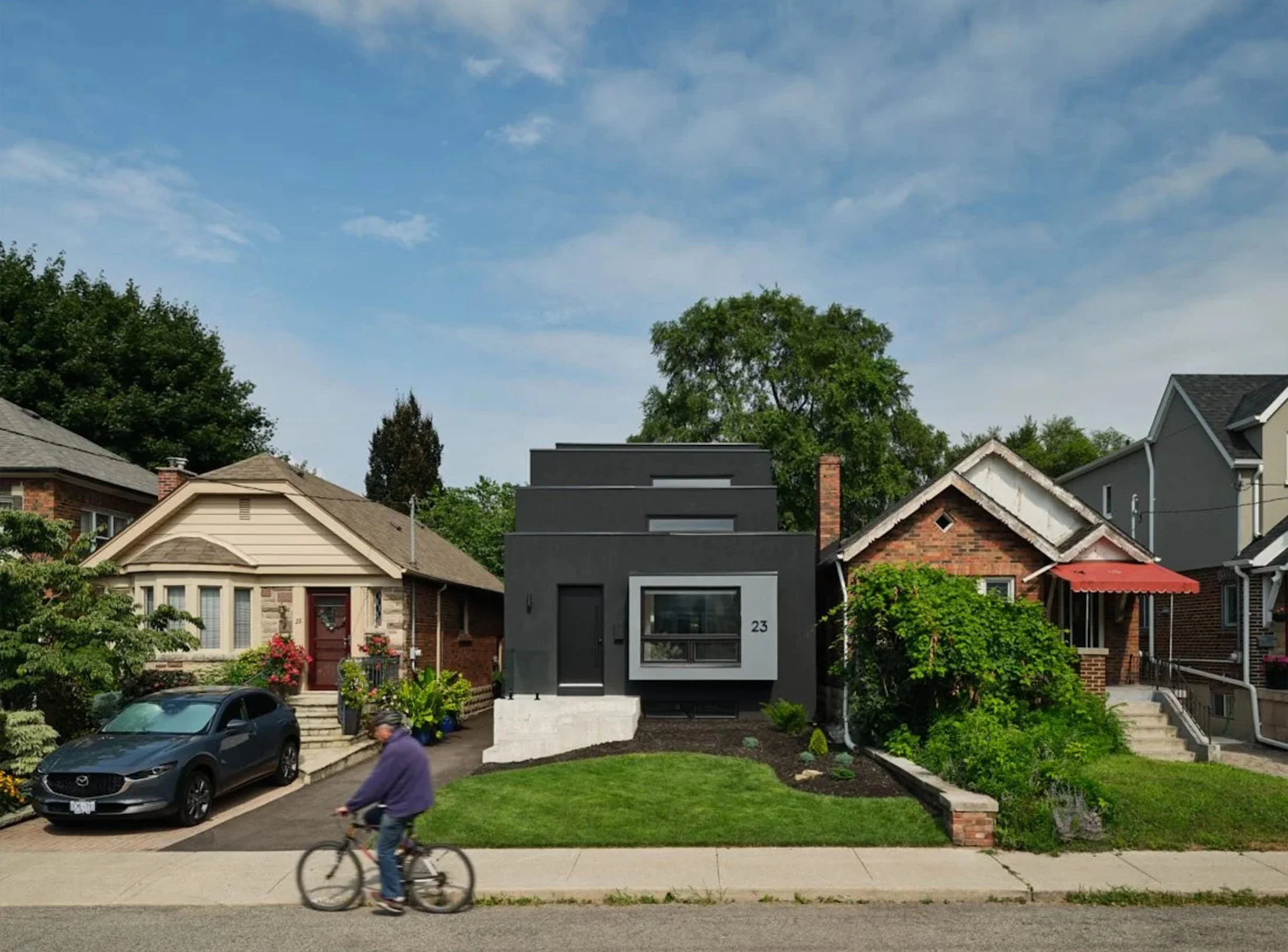 Periscope House exterior in East York, Toronto, built by Maxamin Homes, modern black home with boxy design, front lawn, and cyclist passing by.