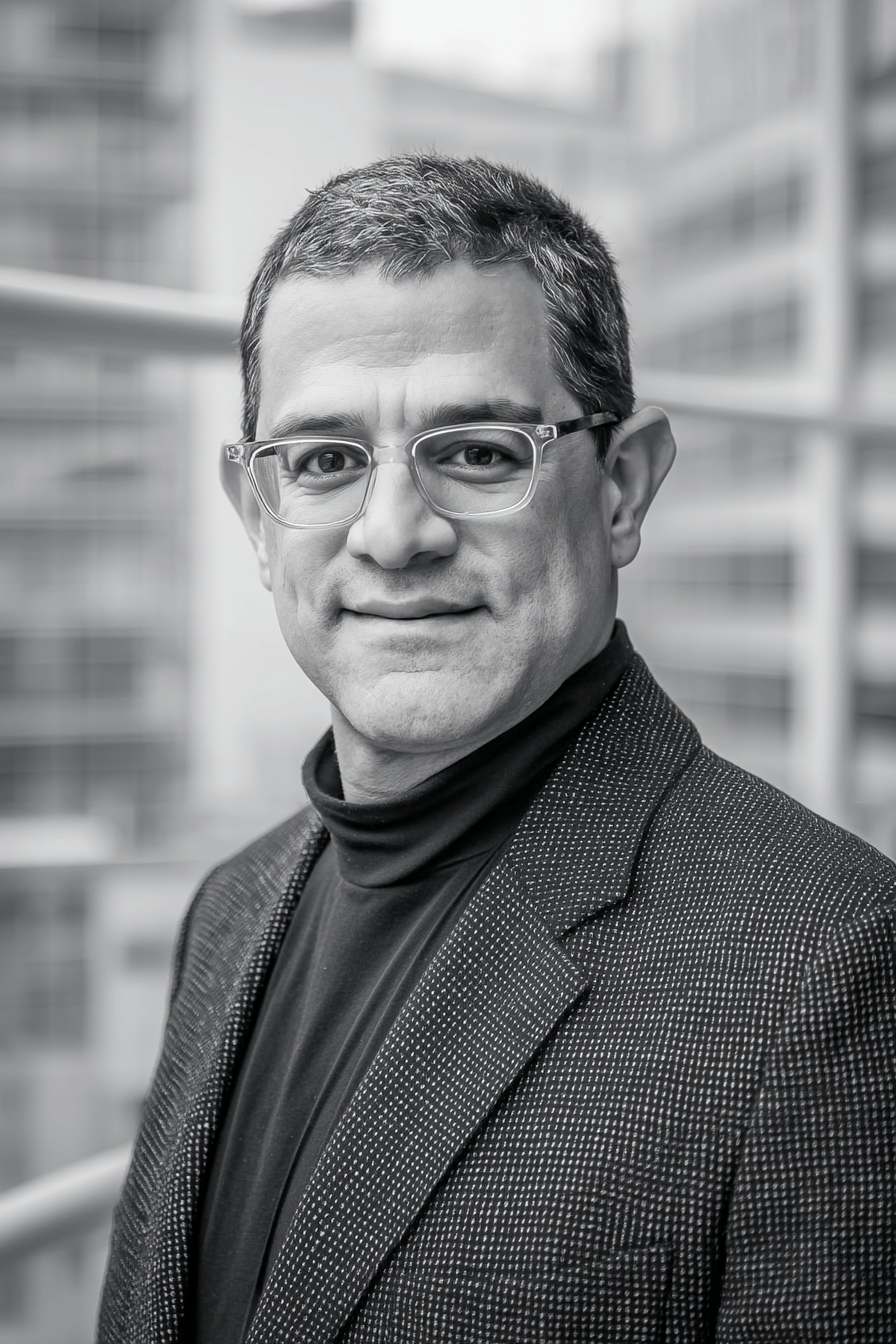 Portrait of Amin Sheivari, Director of Maxamin Homes, in a black and white photo with modern custom home behind him.