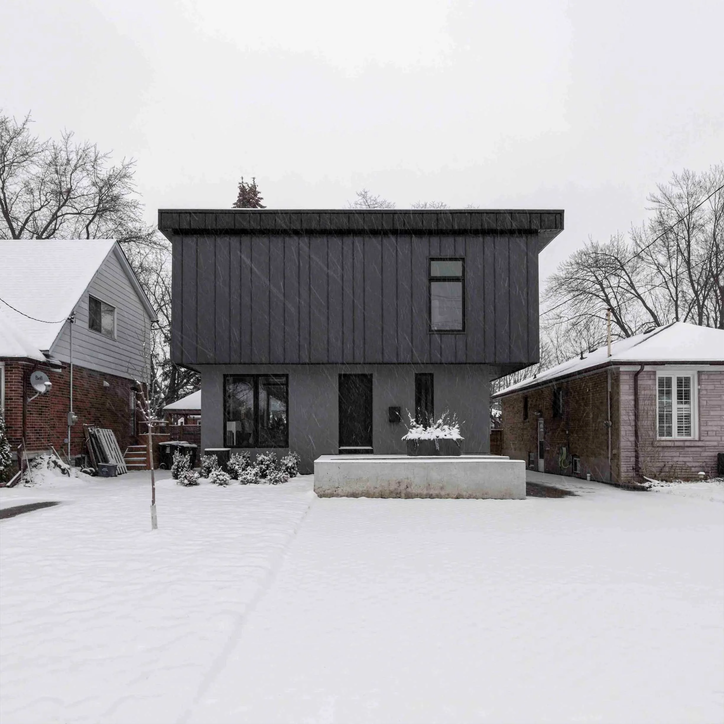 Albers House, a modern two-story home addition and renovation in Scarborough, Toronto, built by Maxamin Homes, featuring a dark upper level, gray lower level, and geometric minimalist design surrounded by snow and winter trees.