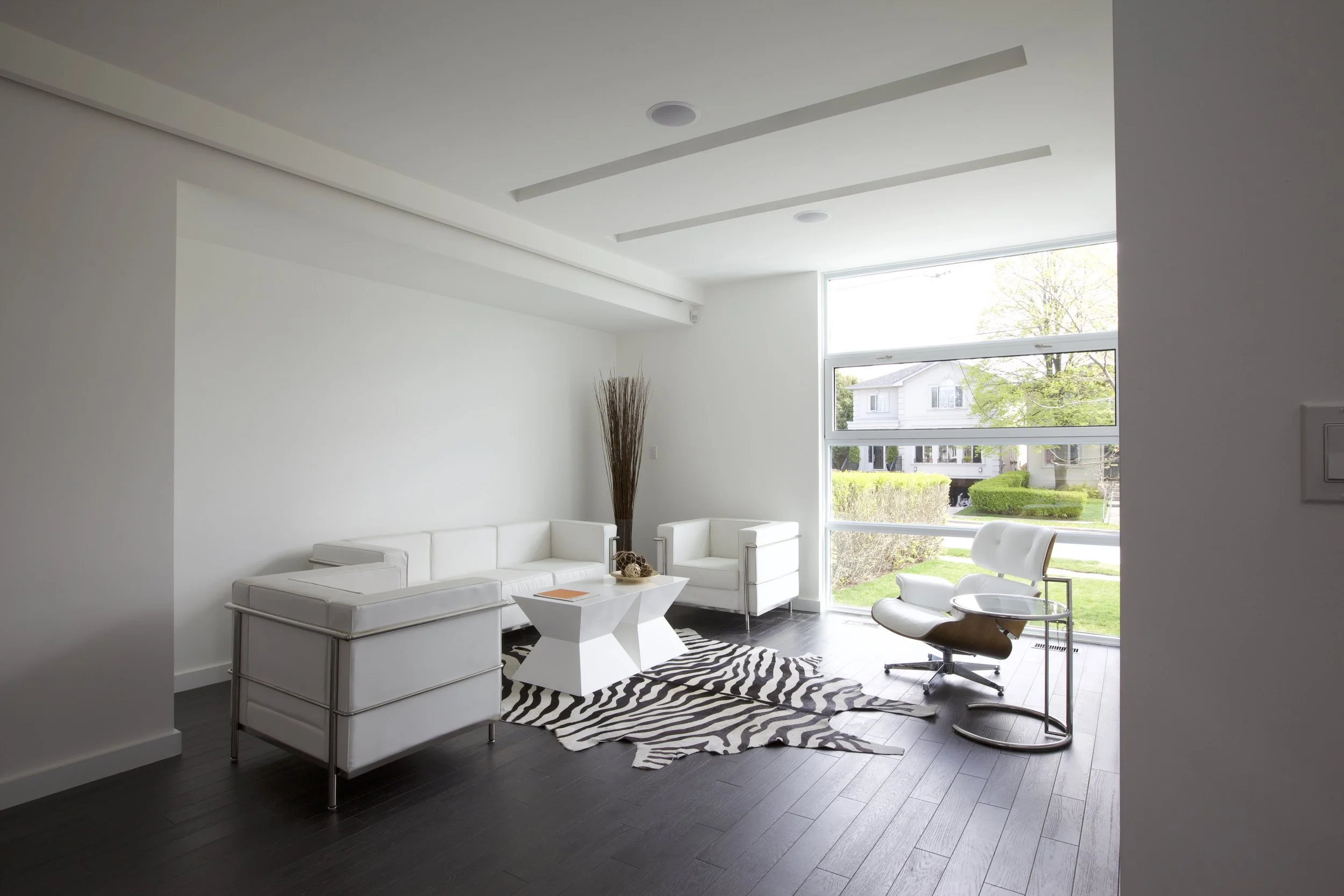 Patio House living room in North York, Toronto, built by Maxamin Homes, with zebra rug, white sofa, chrome lounge chair, and large suburban window view.