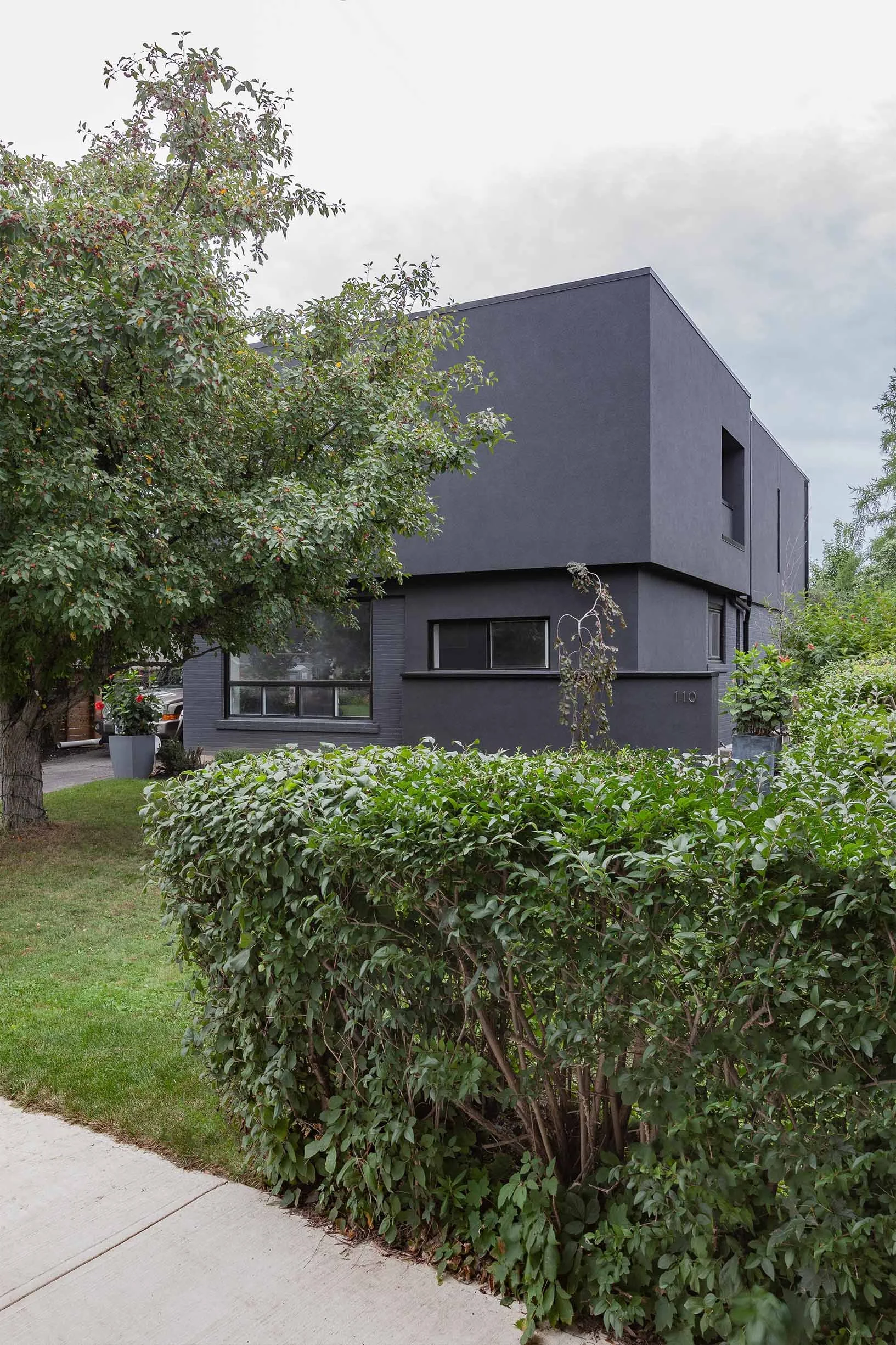 Ebenos House, modern black exterior in North York, Toronto, with rectangular windows, green hedge, and trees built by Maxamin Homes.