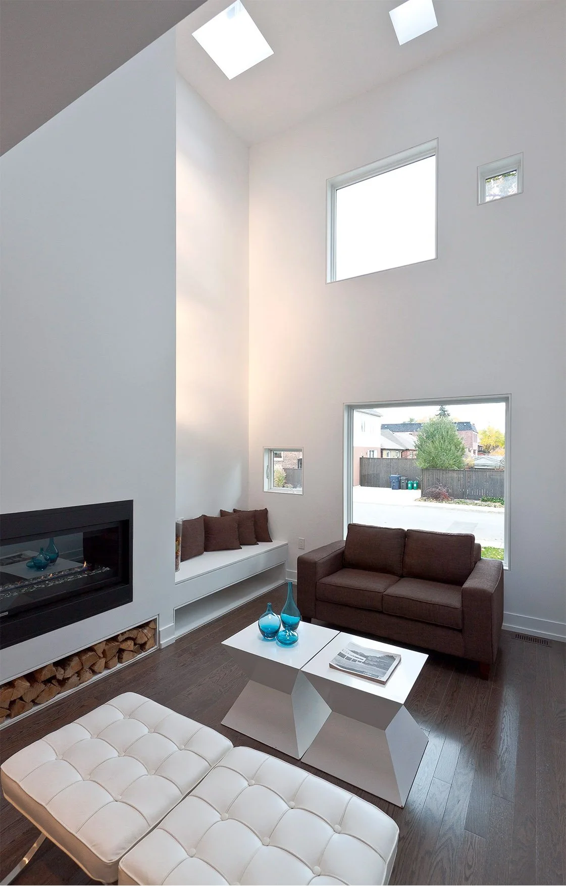Charcoal House living room in East York, Toronto, built by Maxamin Homes, featuring vaulted ceiling, skylights, fireplace, and brown sofa.