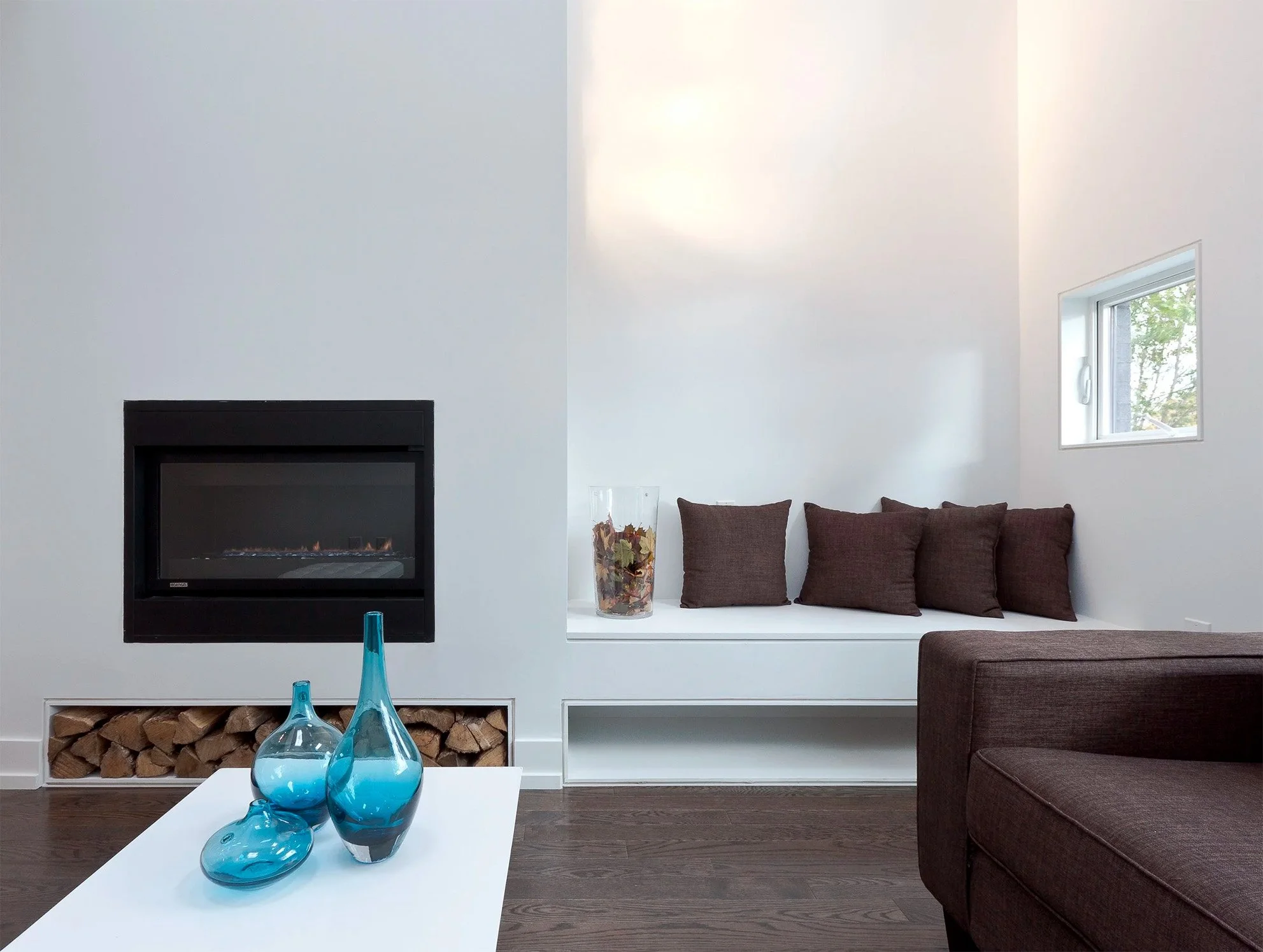 Charcoal House living room in East York, Toronto, built by Maxamin Homes, with fireplace, white walls, brown chair, and coffee table with blue vases.