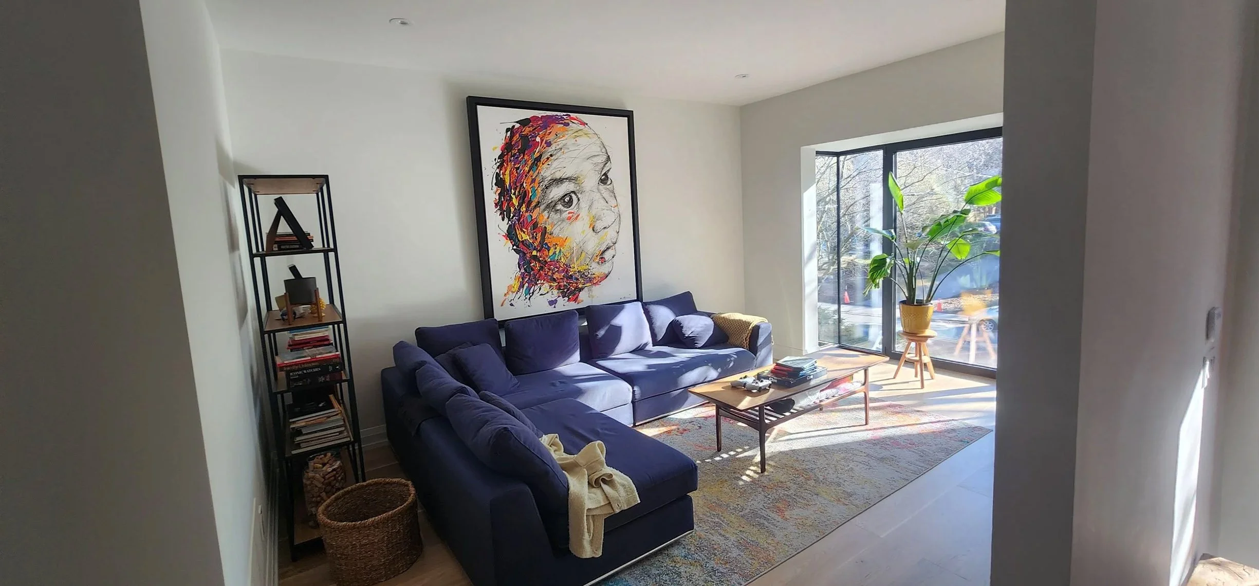 Lantern House living room in The Beaches, Toronto, built by Maxamin Homes, with blue sectional, abstract child portrait, bookshelf, and potted plant.