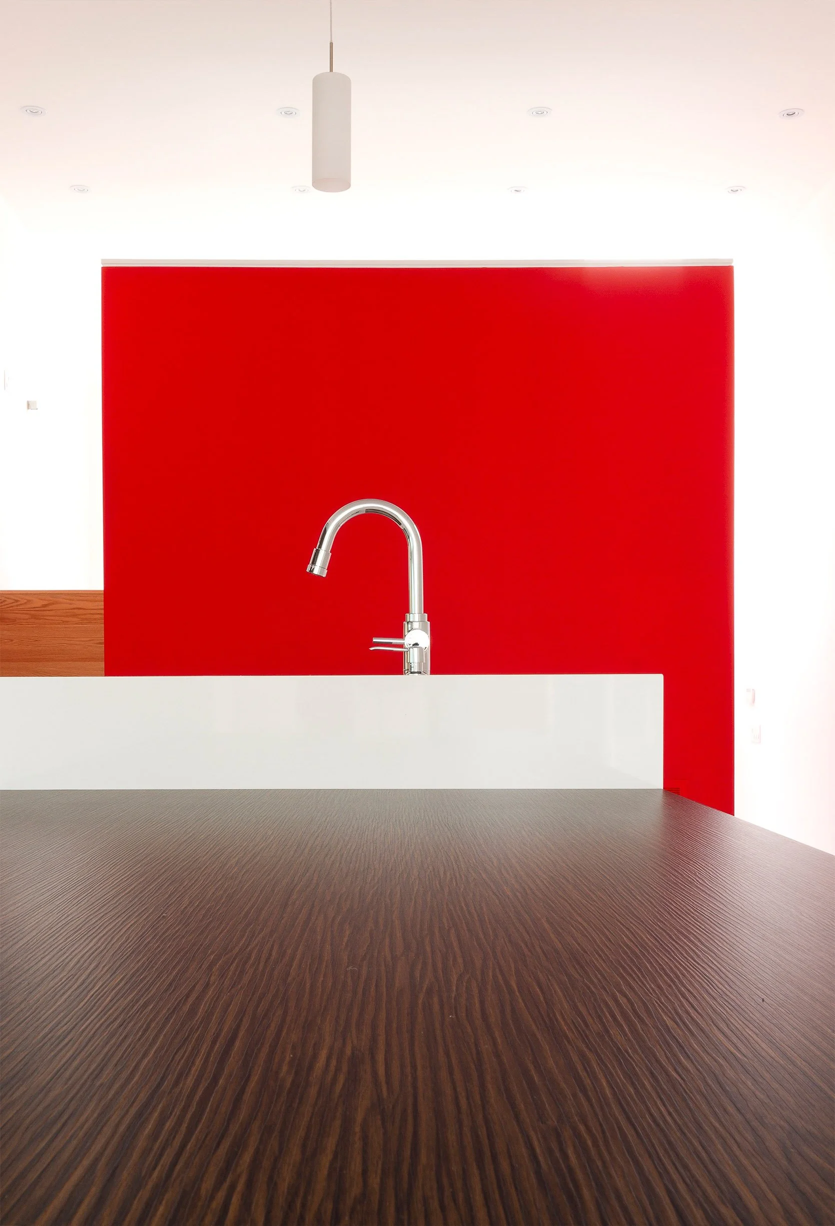 Whale House kitchen in East York, Toronto, built by Maxamin Homes, featuring white counter, stainless faucet, red accent wall, and wood flooring.