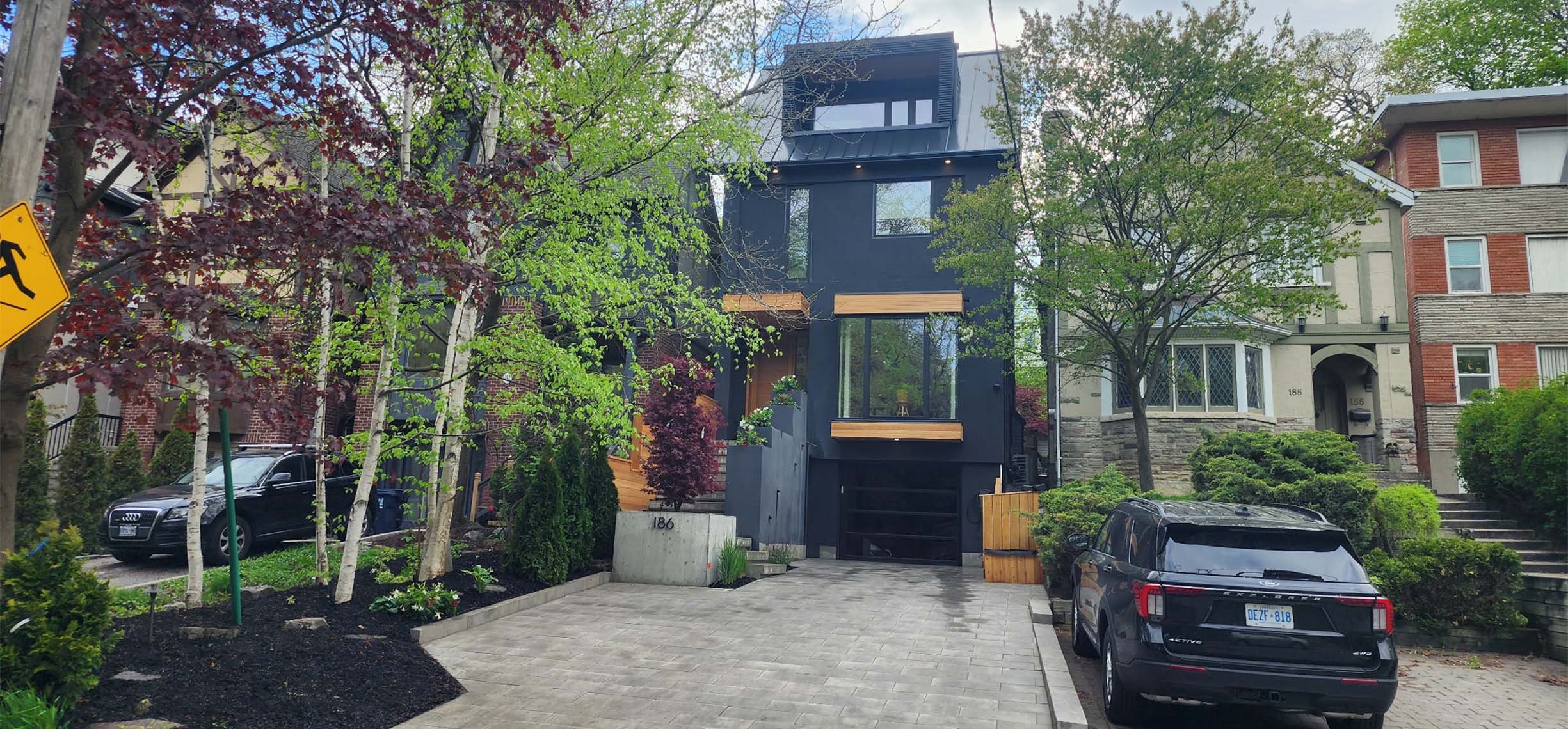Lantern House exterior in The Beaches, Toronto, built by Maxamin Homes, modern black design with large windows, wood accents, and driveway.