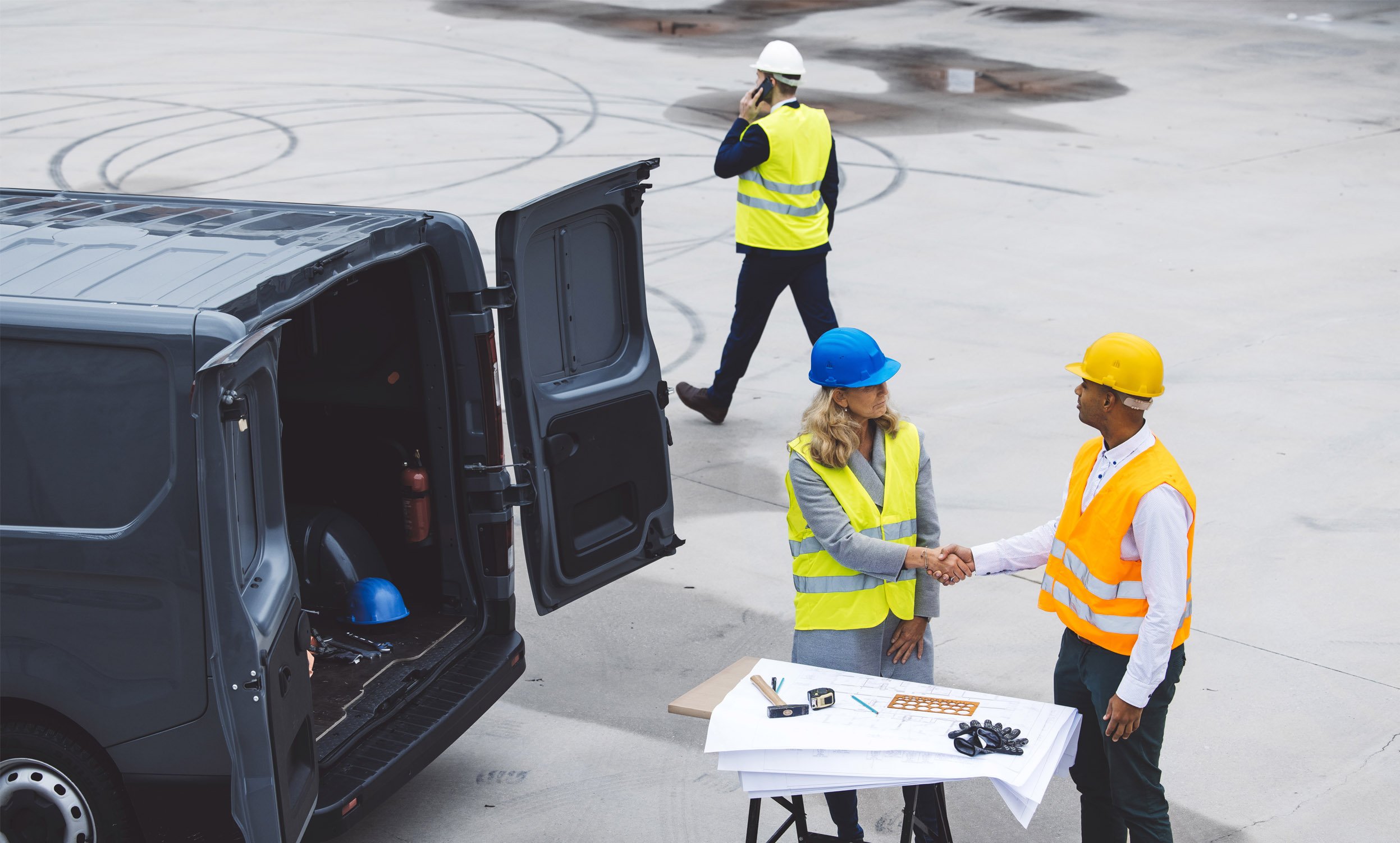 Construction workers in safety gear shaking hands near a van on a construction site.