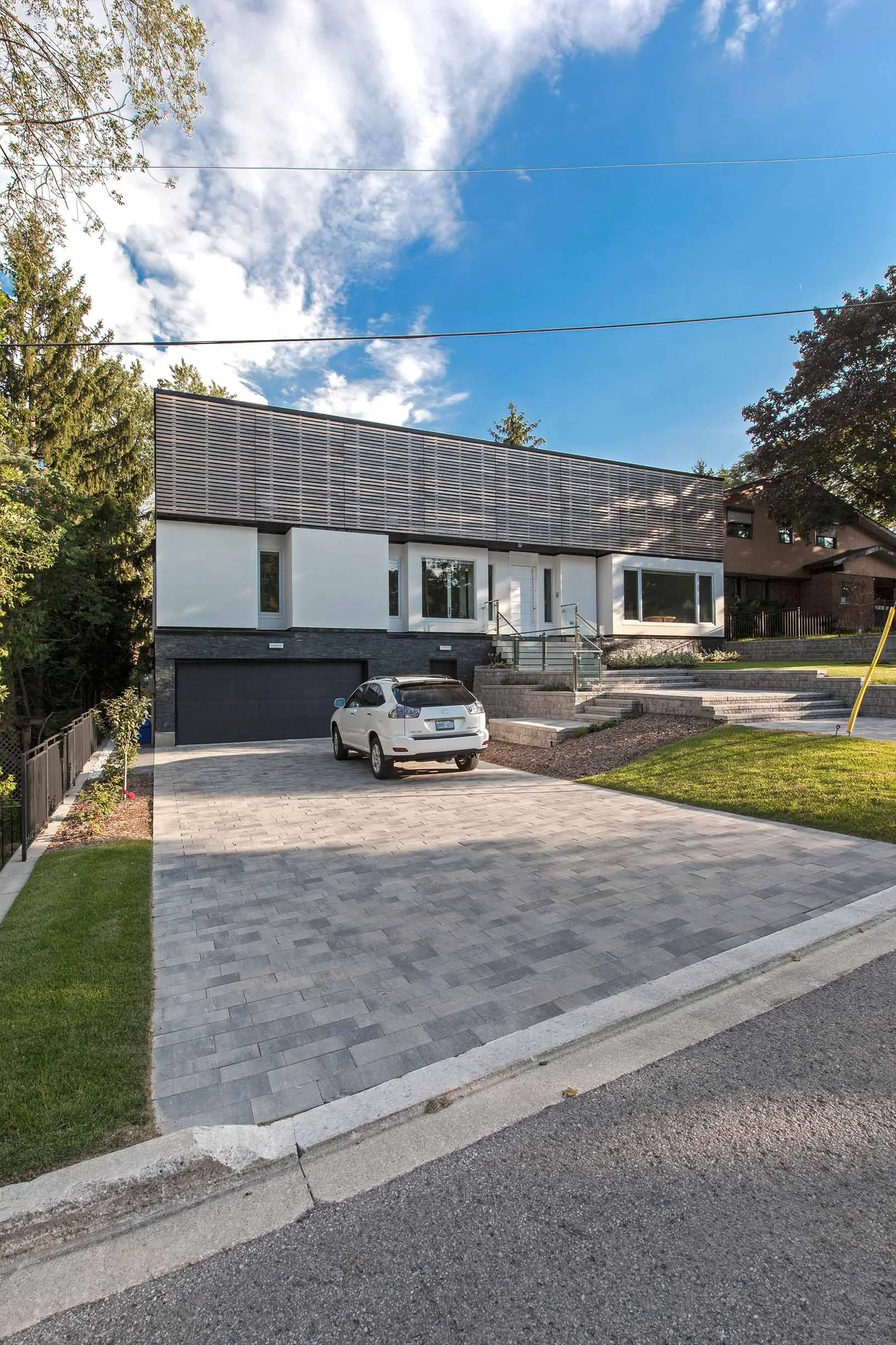 Gallery House exterior in East York, Toronto, built by Maxamin Homes, with gray garage door, stairs to entry, and car parked on paved driveway.