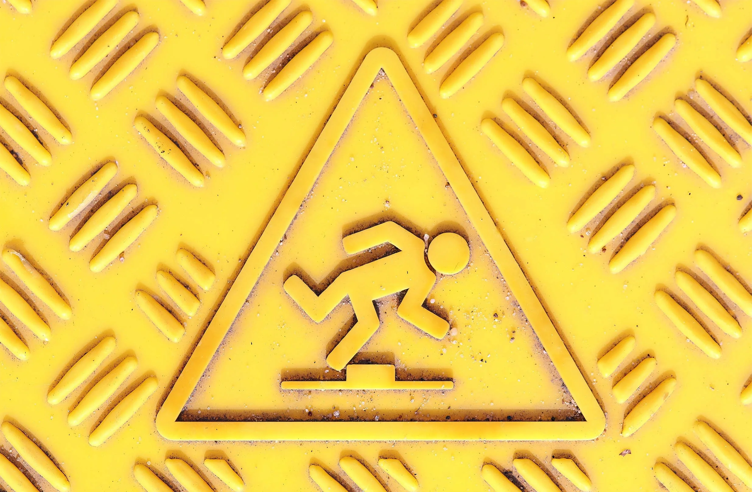 Yellow caution sign with a figure running, indicating caution for slipping or falling, mounted on a yellow grated surface.