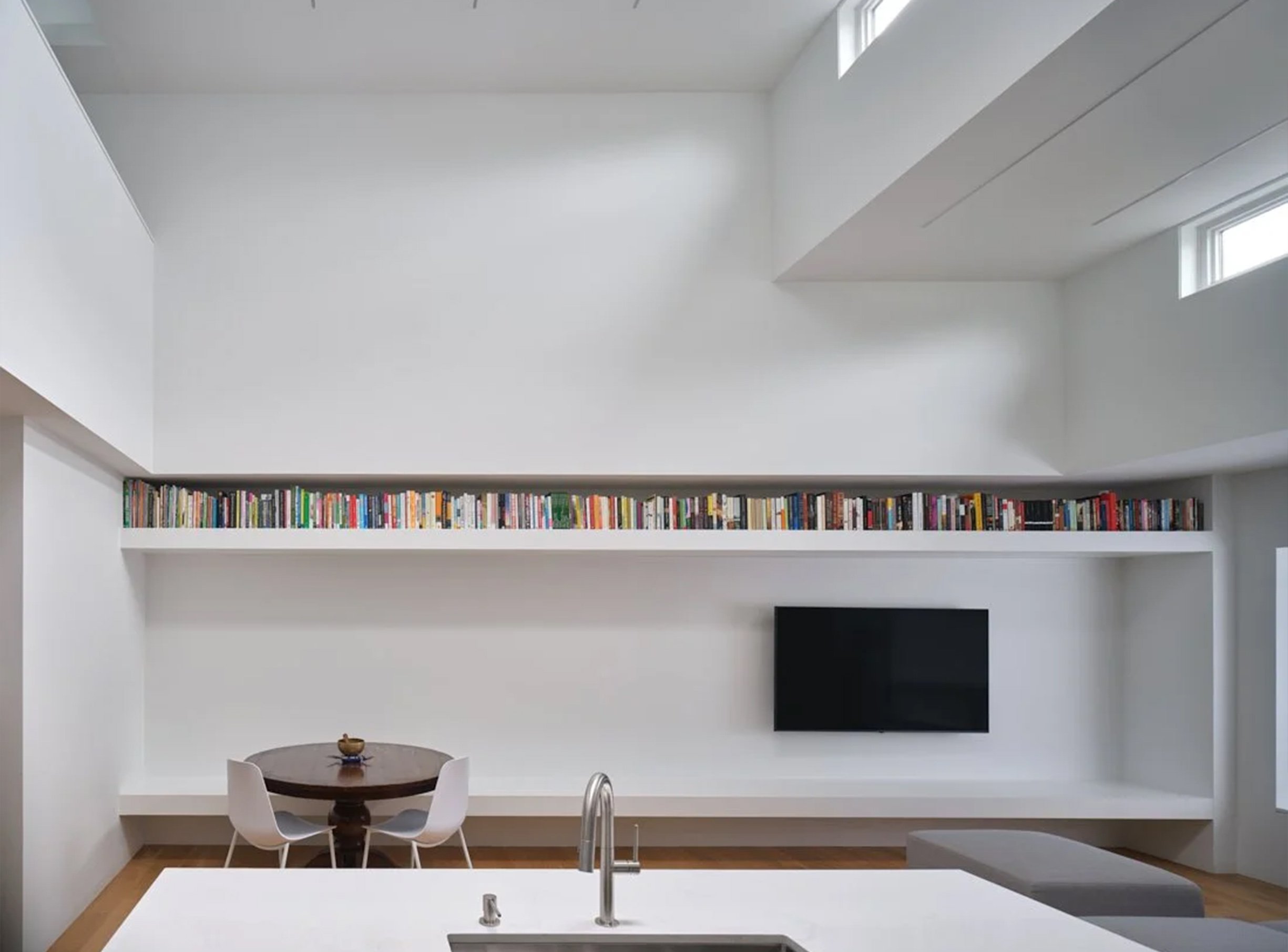 Periscope House living room in East York, Toronto, built by Maxamin Homes, featuring bookshelf, wall TV, round table, and high windows with natural light.