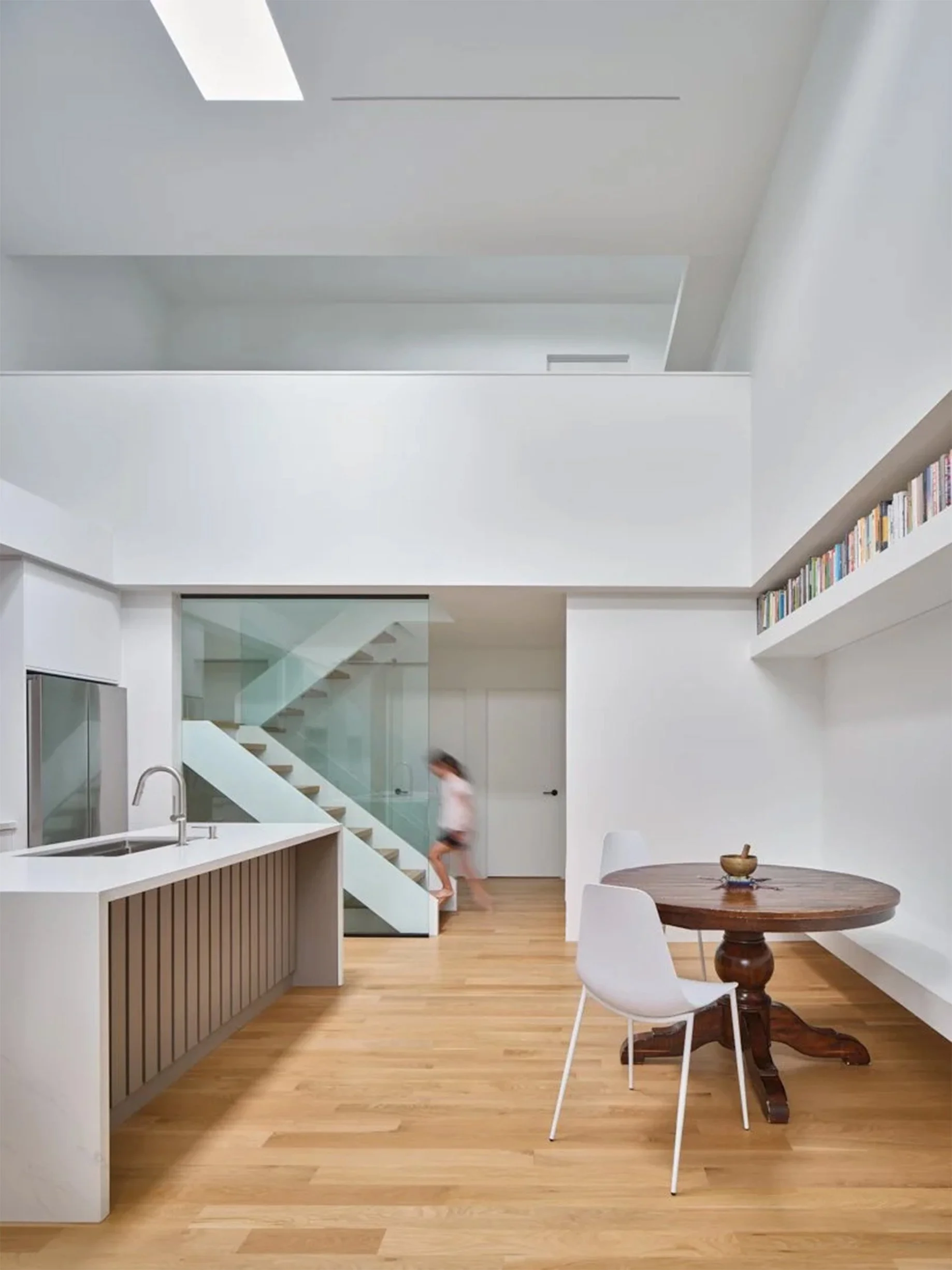 Periscope House kitchen and dining area in East York, Toronto, built by Maxamin Homes, with round table, white chairs, glass staircase, and hardwood floors.