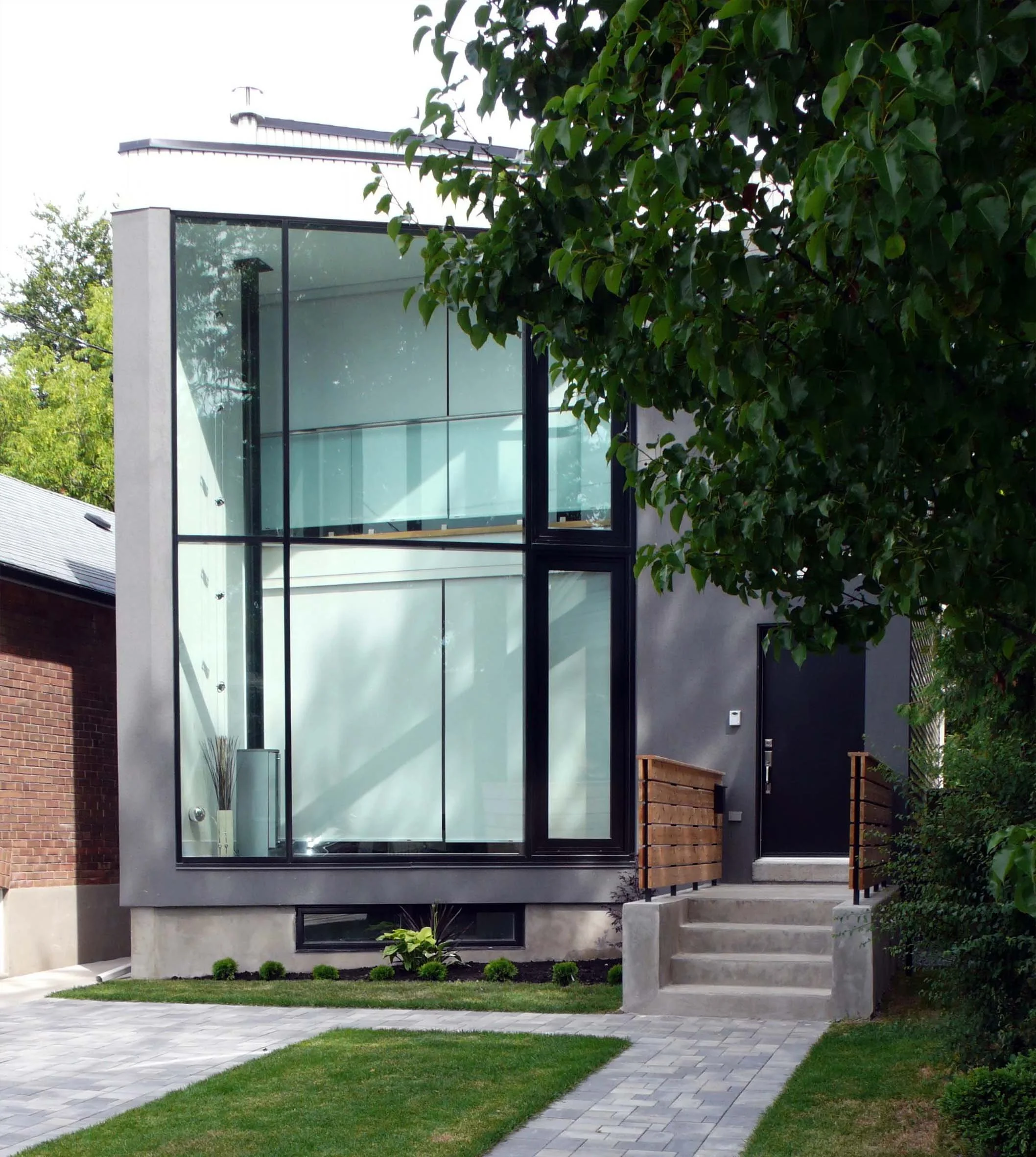 63˚ House, a modern two-story custom home in East York, Toronto, built by Maxamin Homes, featuring gray exterior, large windows, black front door, and paved walkway.