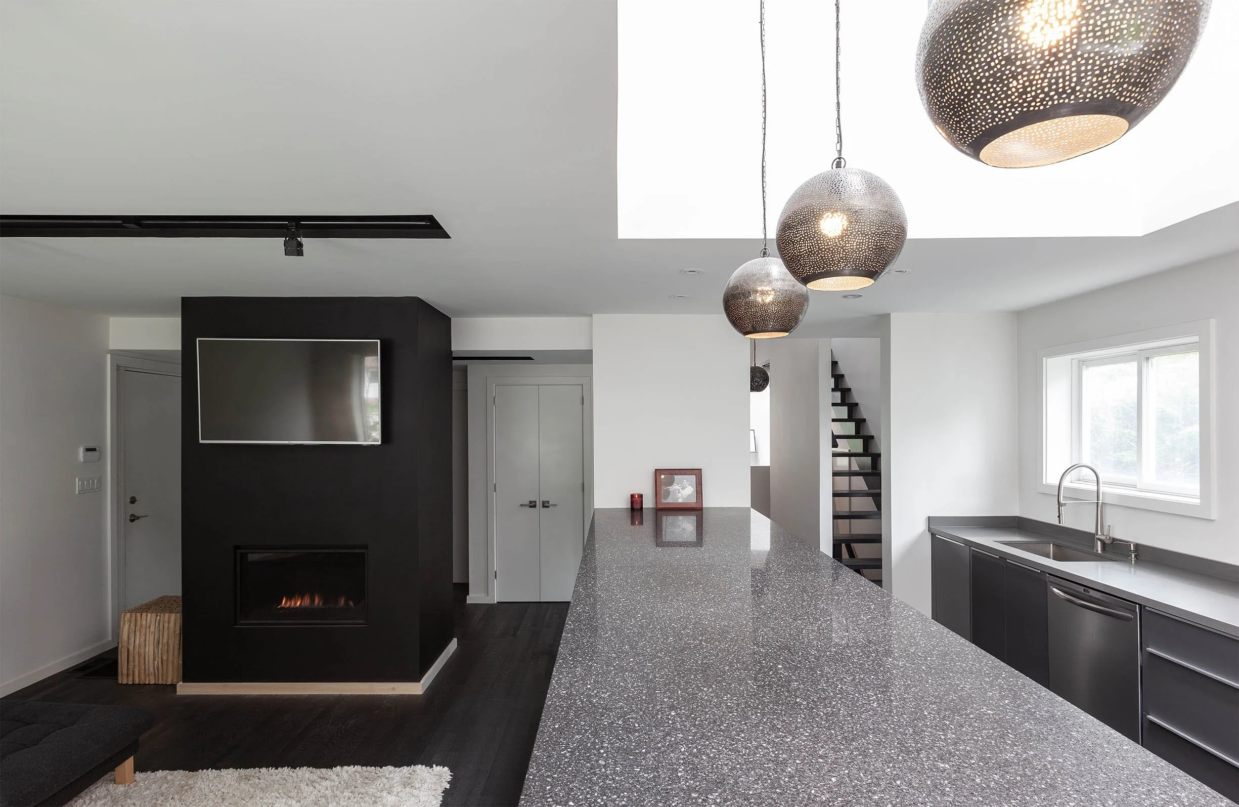 Ebenos House, a modern kitchen and living area in North York, Toronto, with pendant lights, black and white palette, and a sleek fireplace built by Maxamin Homes.