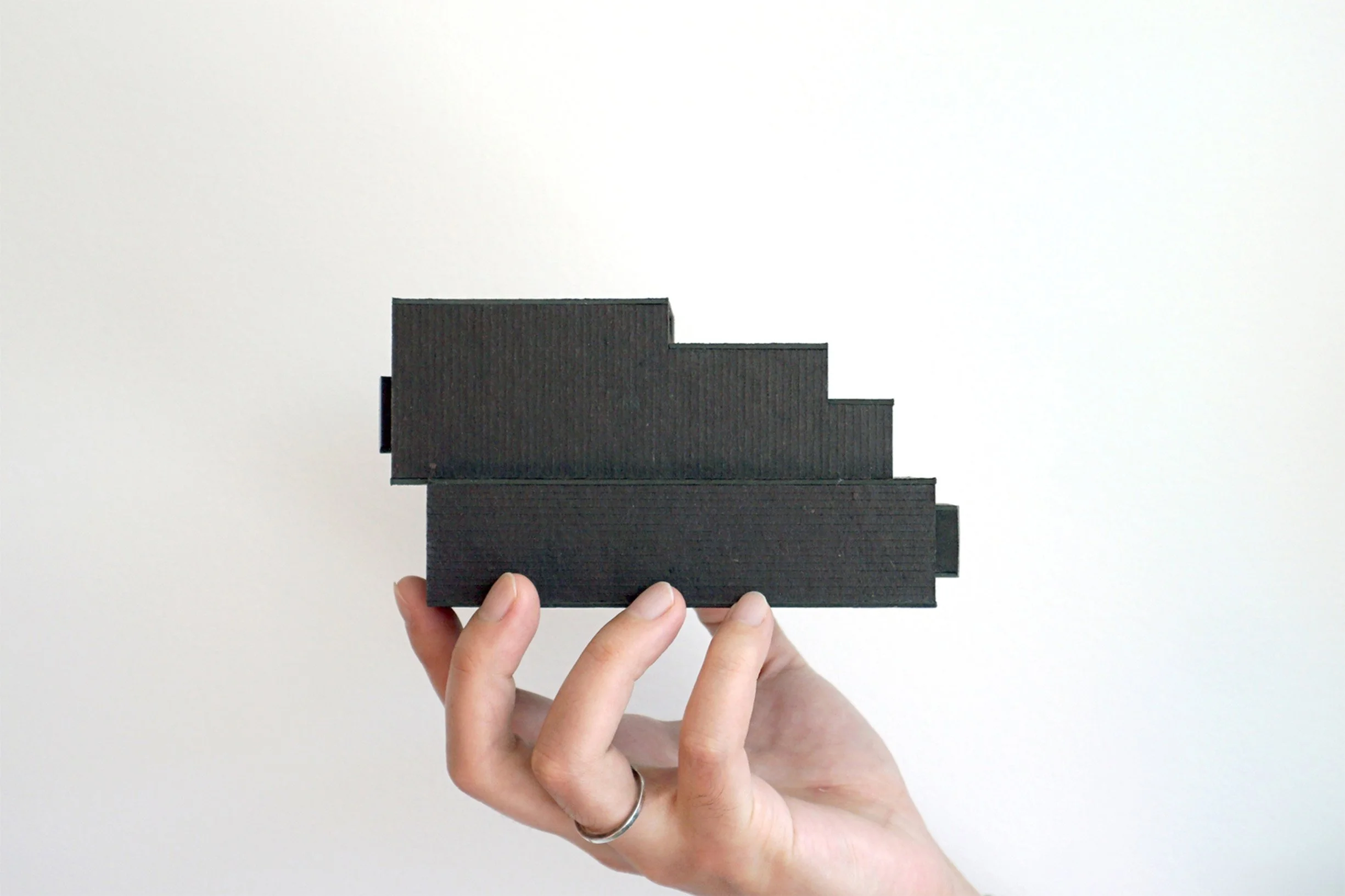 A person's hand holding a small black architectural model against a white background.