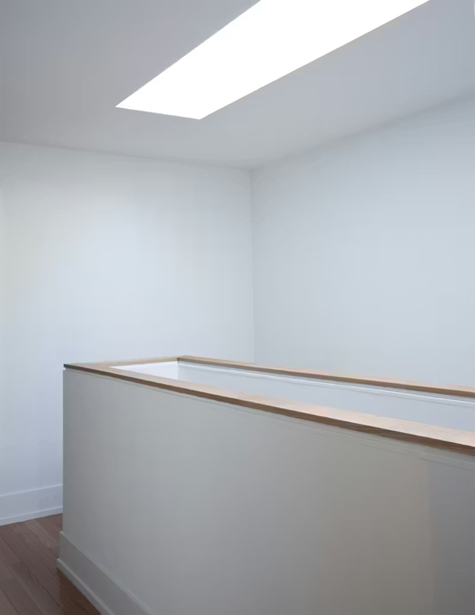 Empty white room with wooden handrail and ceiling light panel.