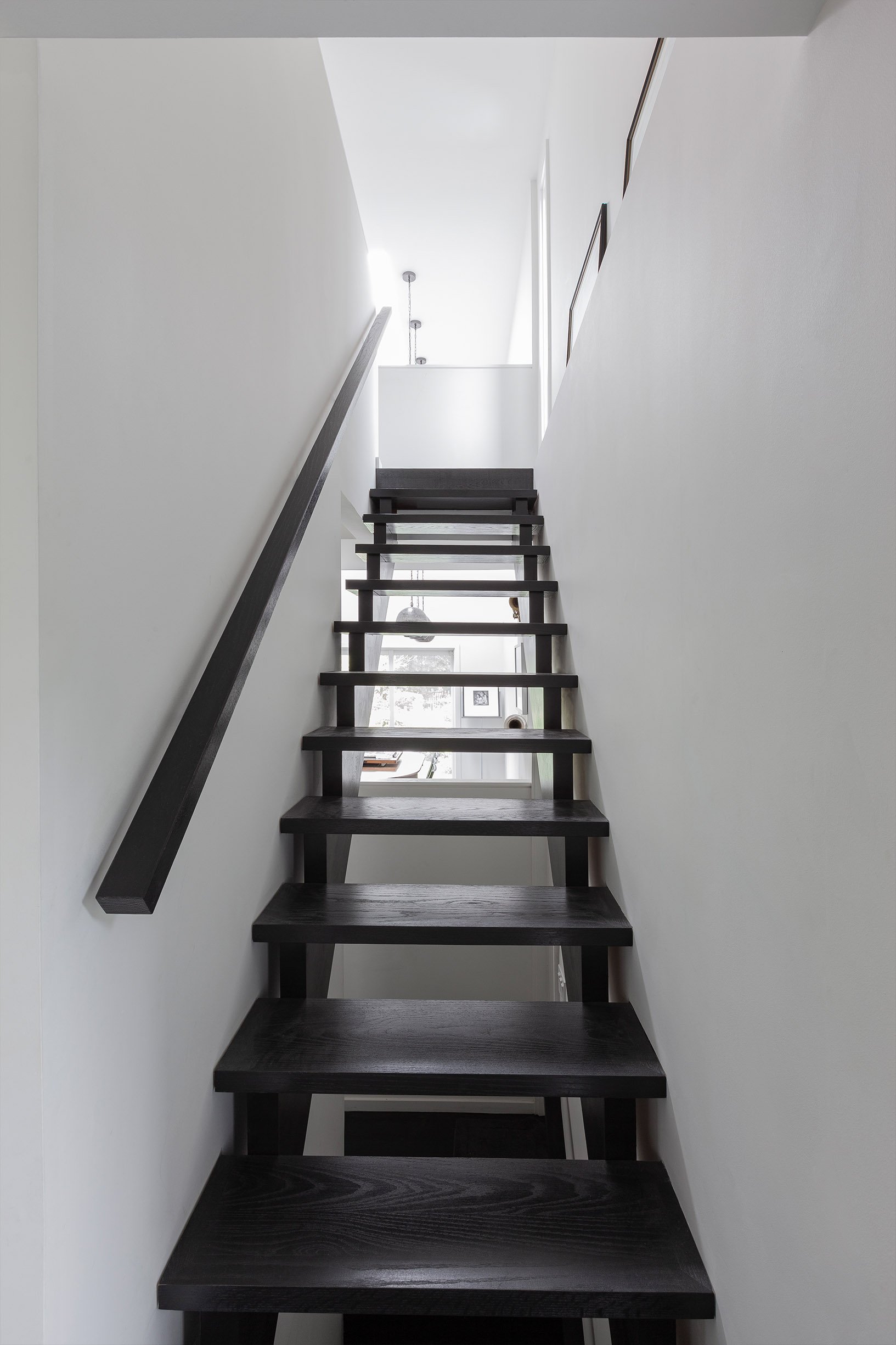 Ebenos House, an interior staircase in North York, Toronto, with dark wooden steps, black handrail, and pendant lights on the upper level built by Maxamin Homes.