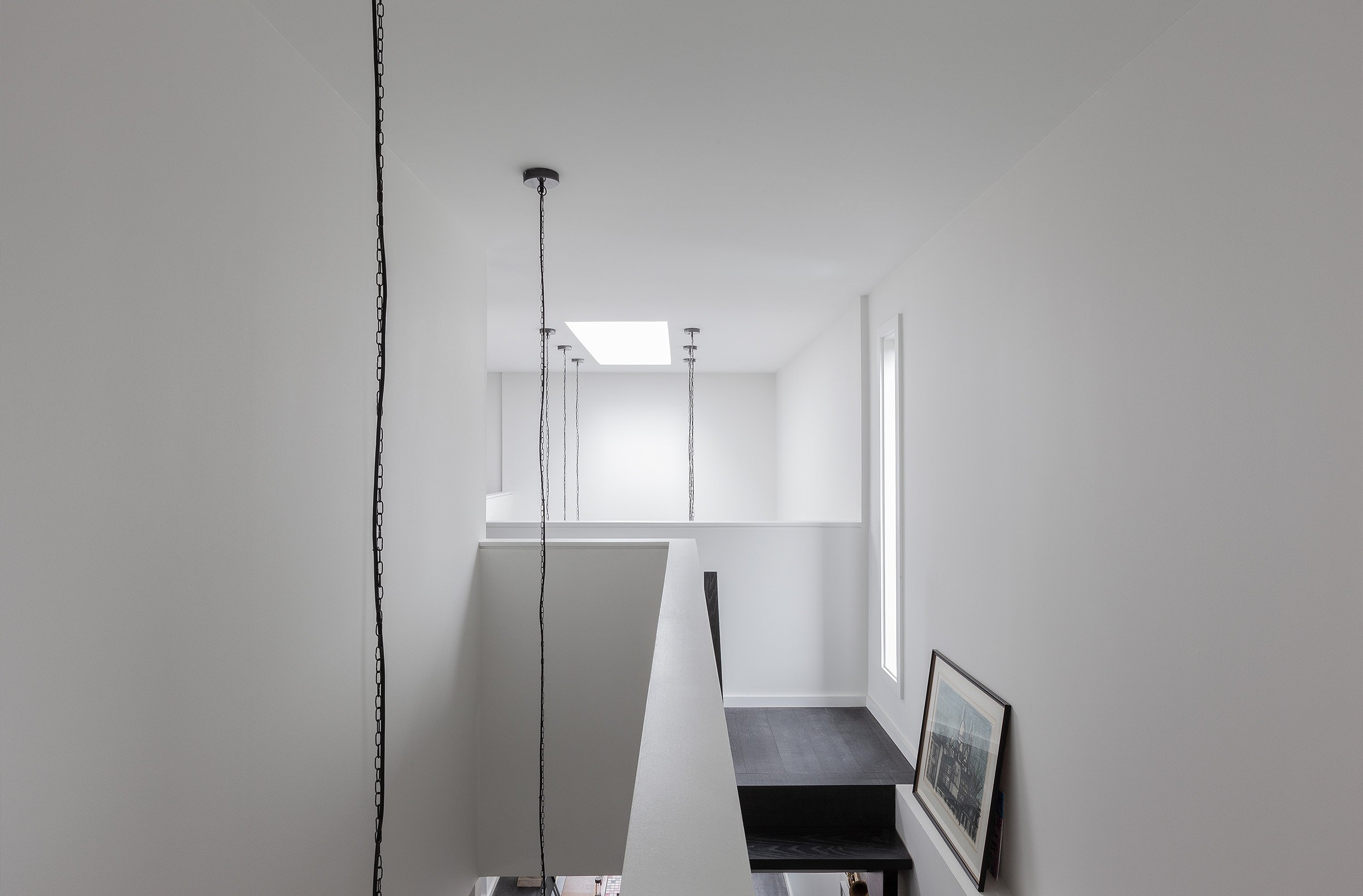 Ebenos House, a minimalist stairway area in North York, Toronto, with black steps, white walls, framed artwork, and skylight illumination built by Maxamin Homes.