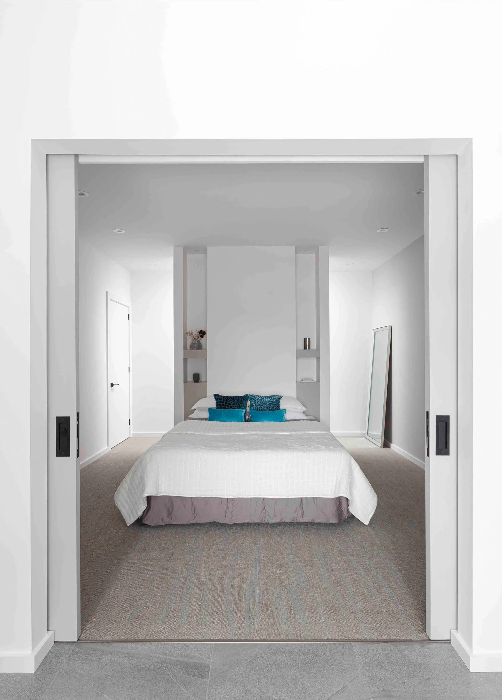 Albers House bedroom in Scarborough, Toronto, built by Maxamin Homes, with white walls, gray bedding, teal pillows, and leaning mirror.