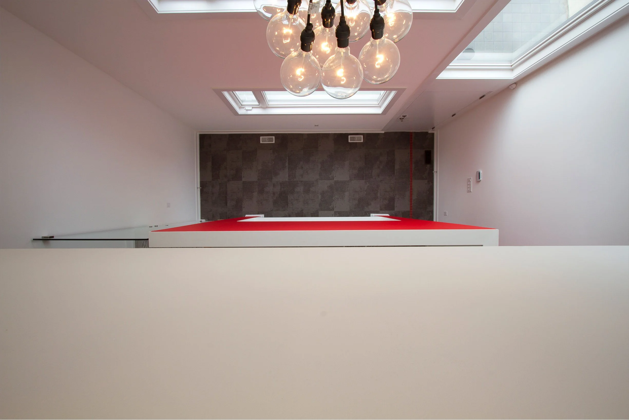 Whale House interior in East York, Toronto, built by Maxamin Homes, with glass bulb chandelier, skylights, gray wall, and red carpeted platform.