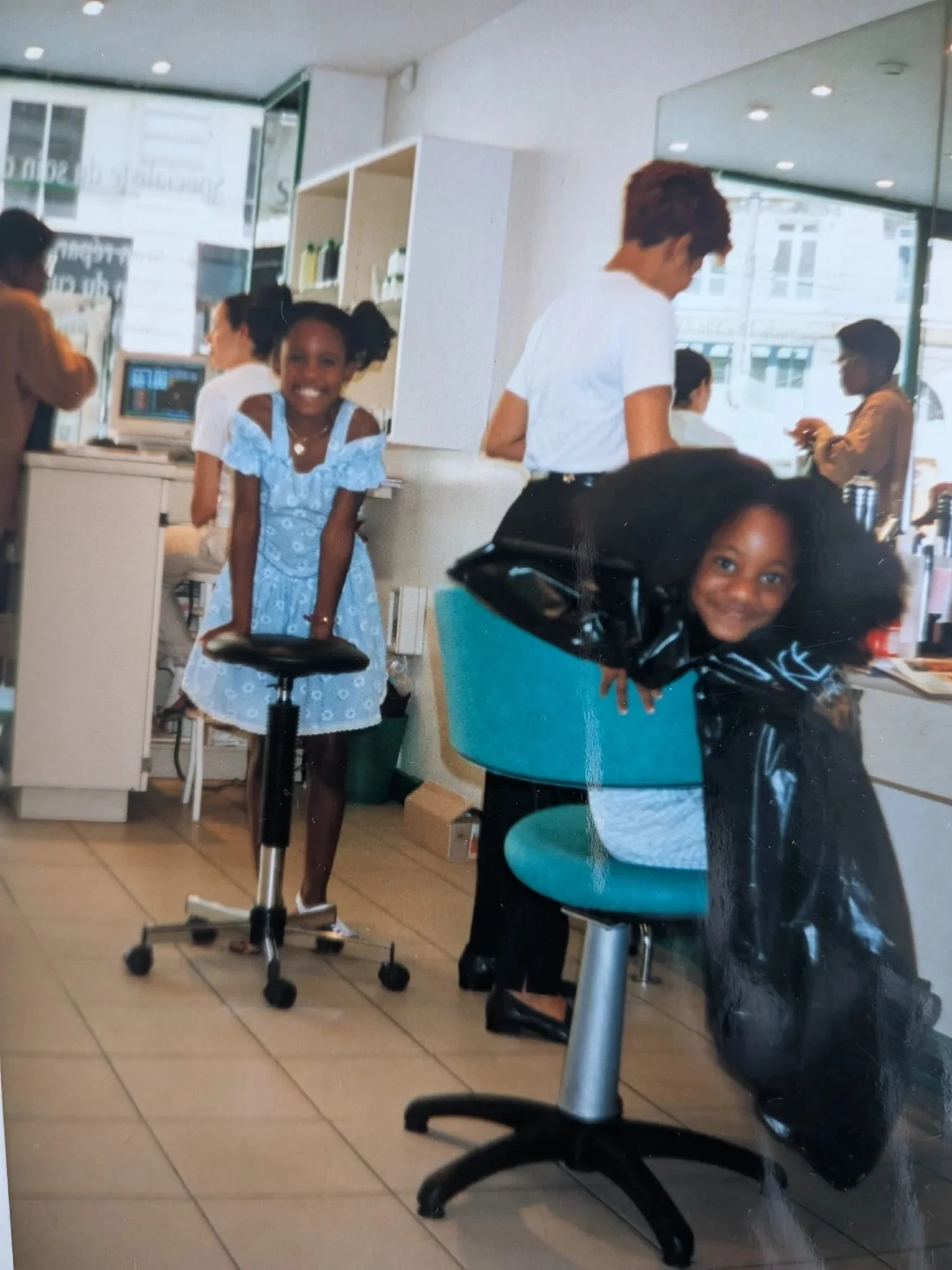 Deux jeunes filles souriantes dans une coiffure avec des personnes travaillant en arrière-plan dans un salon de coiffure.