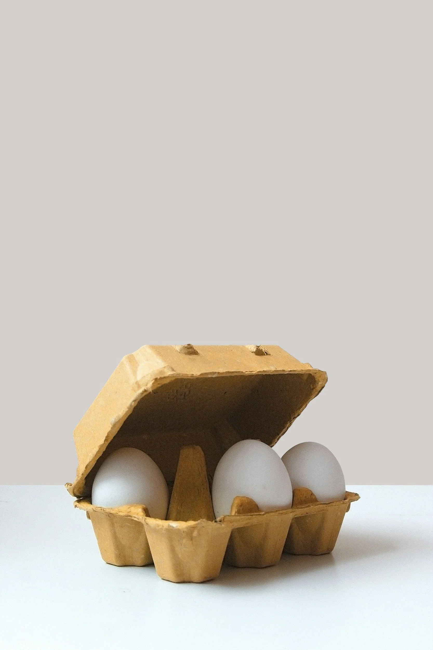 Eggs in a cardboard egg carton with some eggs missing, on a white surface against a gray background.