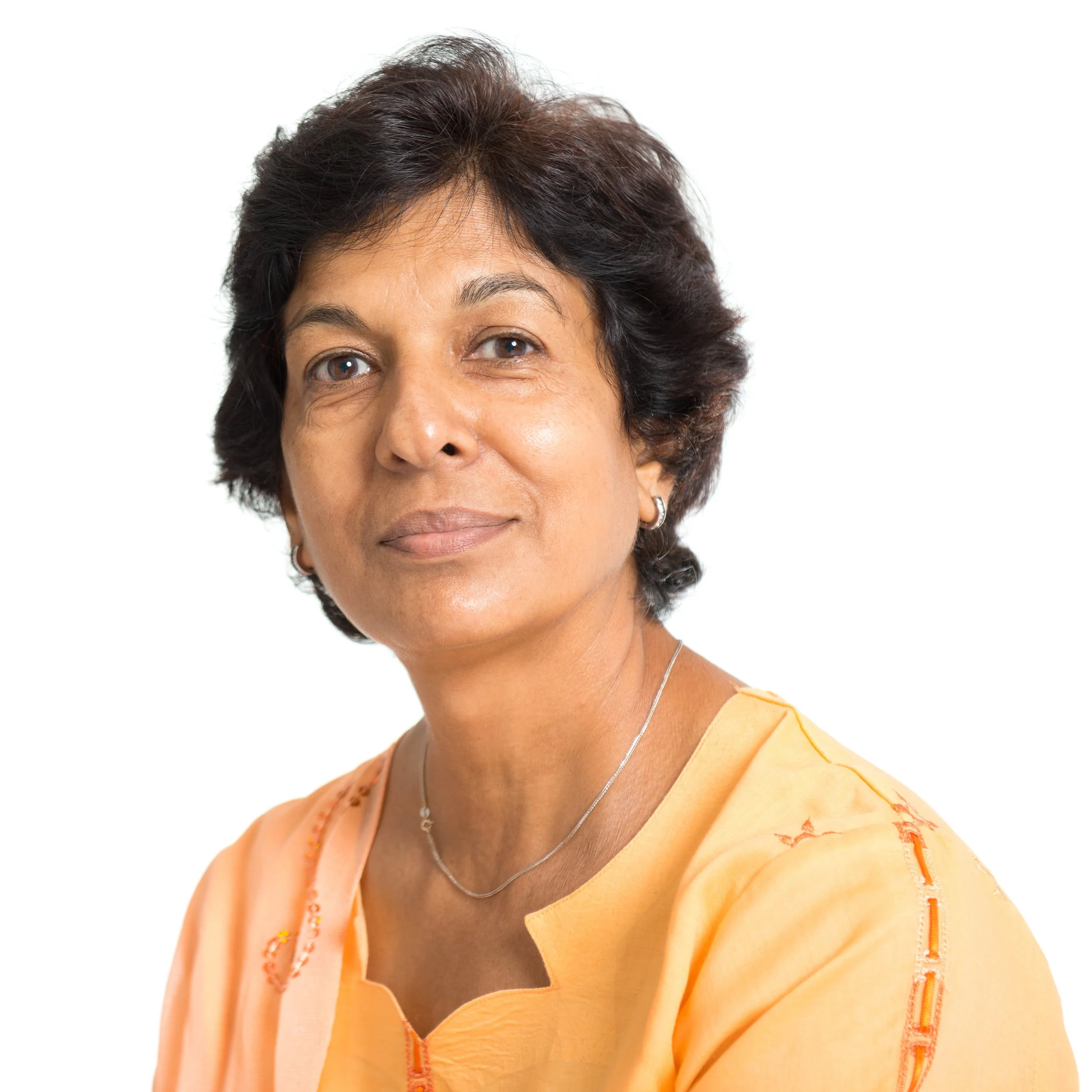 Close-up of a middle-aged woman of color with short dark hair and tan skin wearing a yellow top with a zip, silver earrings, and a silver necklace, smiling softly against a plain white background.