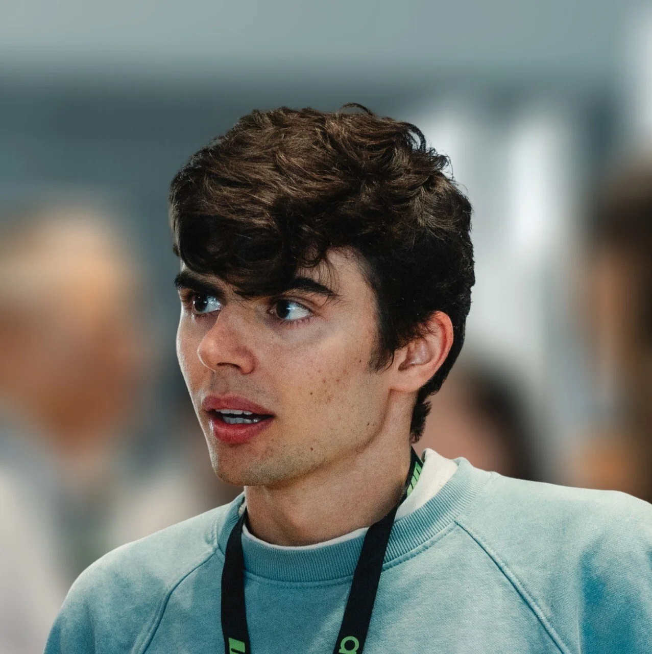 A portrait of Alexis Sursock: A young man with curly brown hair wearing a light blue sweatshirt.