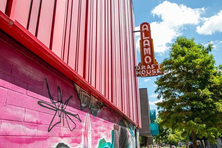 Exterior of Alamo Drafthouse Cinema with red panel walls and mural art on a sunny day