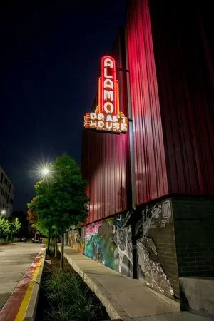Illuminated vintage-style Alamo Drafthouse Cinema sign glowing at night on a red-paneled building