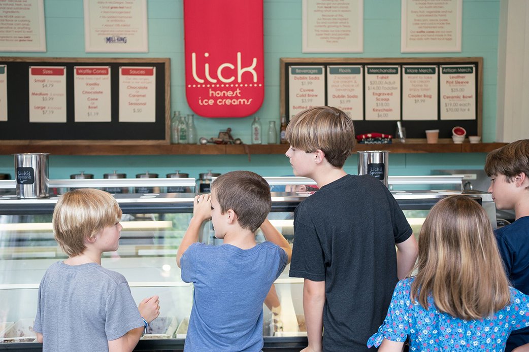 Children selecting flavors at Lick Honest Ice Creams shop with menu boards in the background