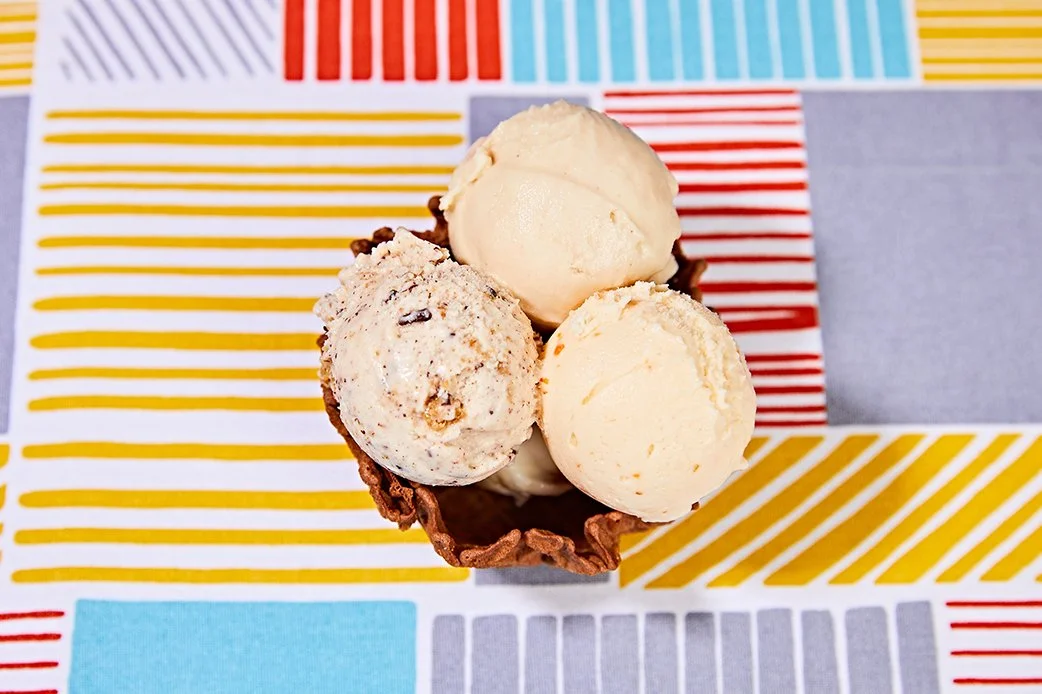 Three scoops of artisan ice cream in a waffle bowl from Lick Honest Ice Creams on a colorful tablecloth
