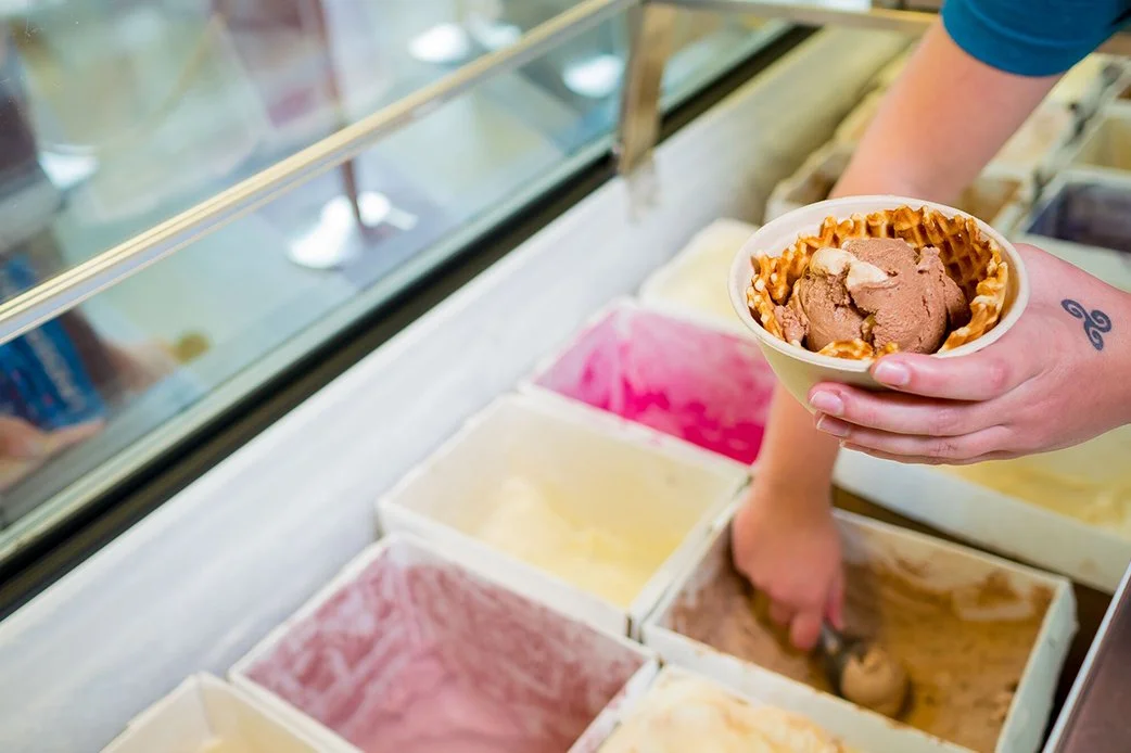 Scoop of chocolate ice cream in a waffle bowl being served from Lick Honest Ice Creams display case