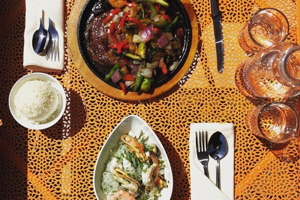 Overhead view of sizzling steak with vegetables, rice, and seafood salad on an outdoor patterned table