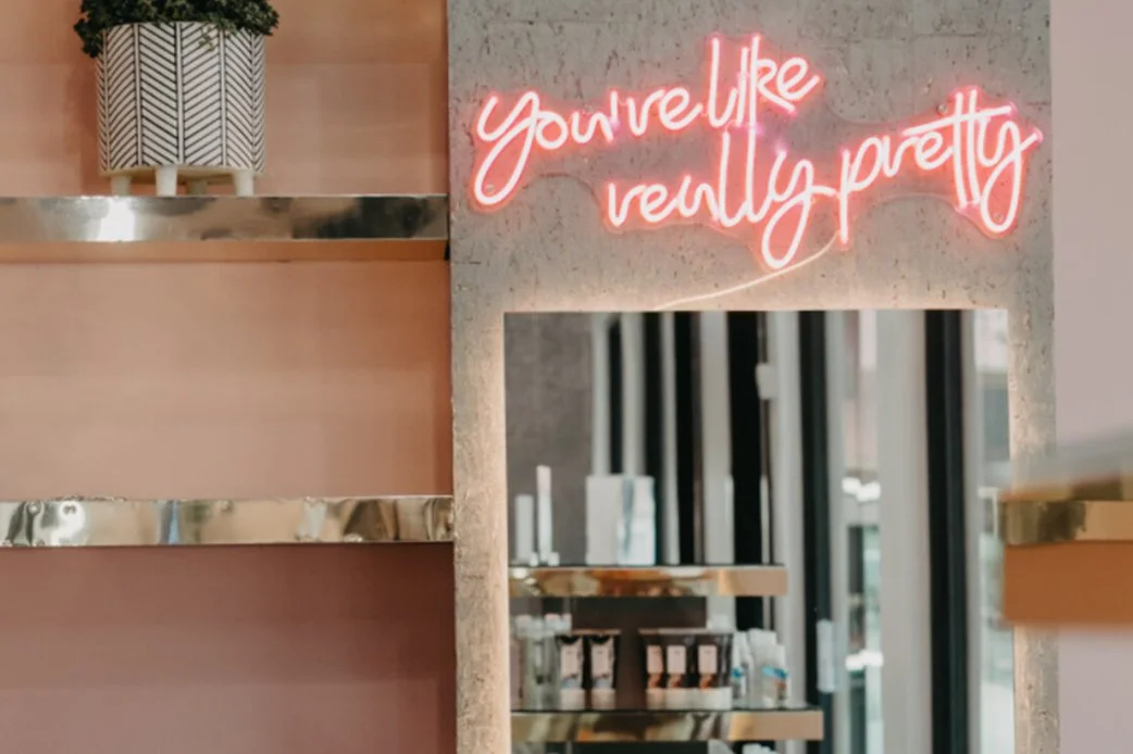 Neon sign reading 'you're like really pretty' above a mirror inside The Collective ATX salon