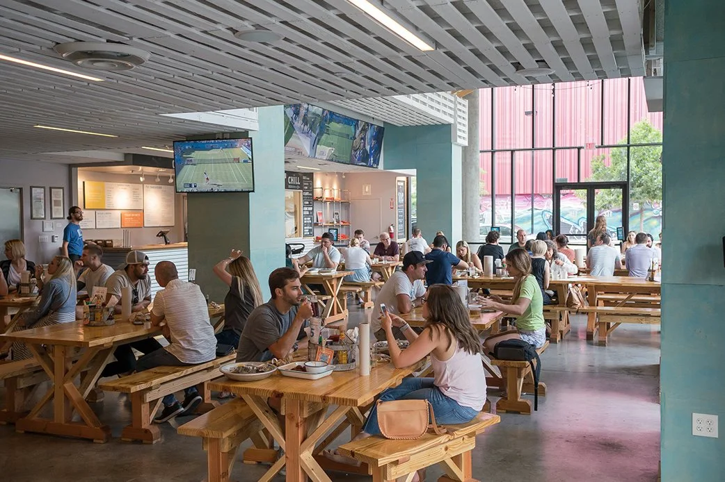 Guests dining indoors at TLC Lamar Union at communal wooden tables
