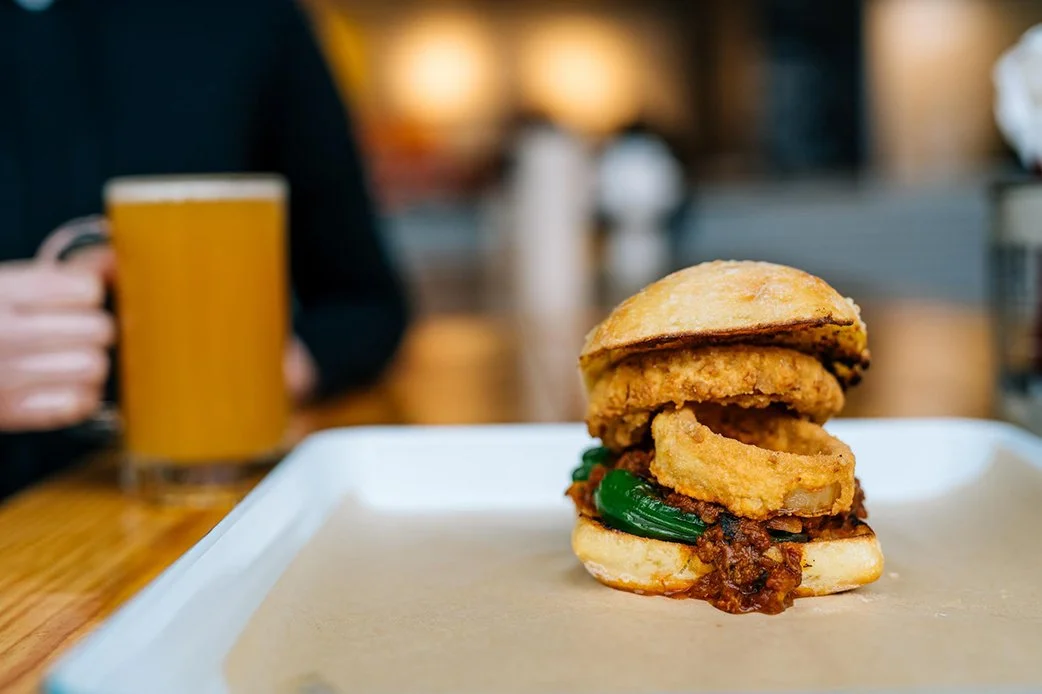 Burger with onion rings and peppers on a bun served on a tray at TLC Lamar Union