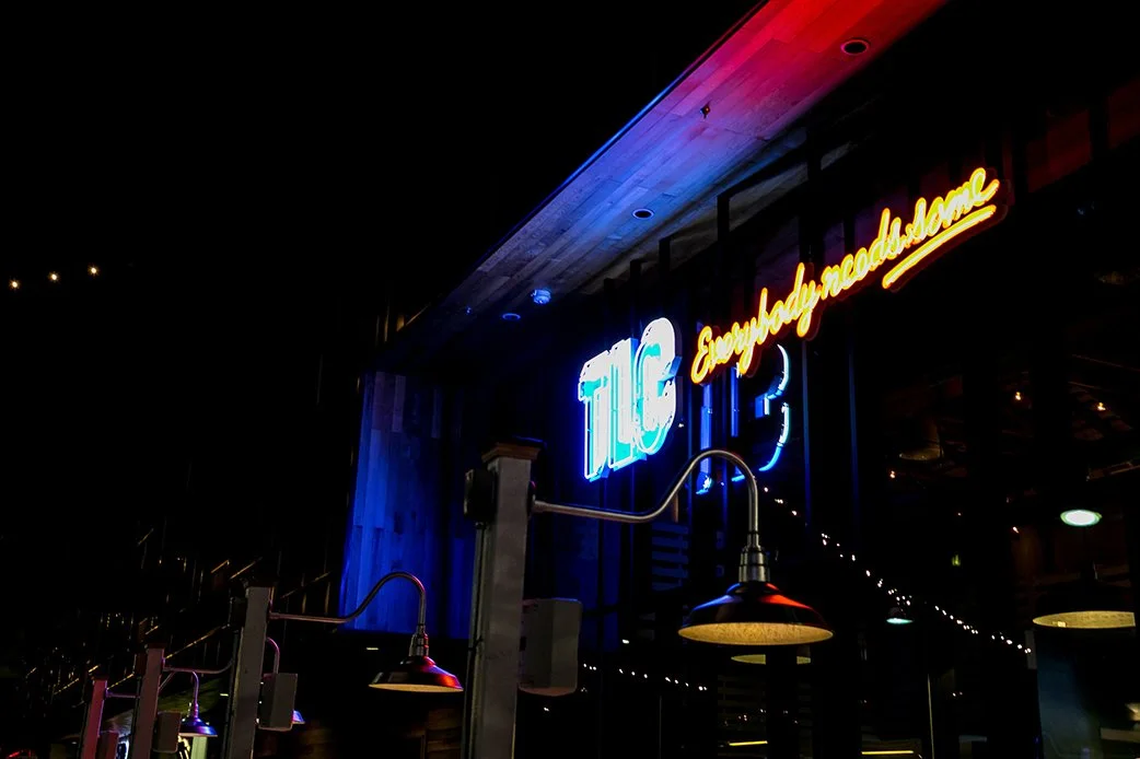Neon TLC sign at night reading Everybody Needs Some at Lamar Union