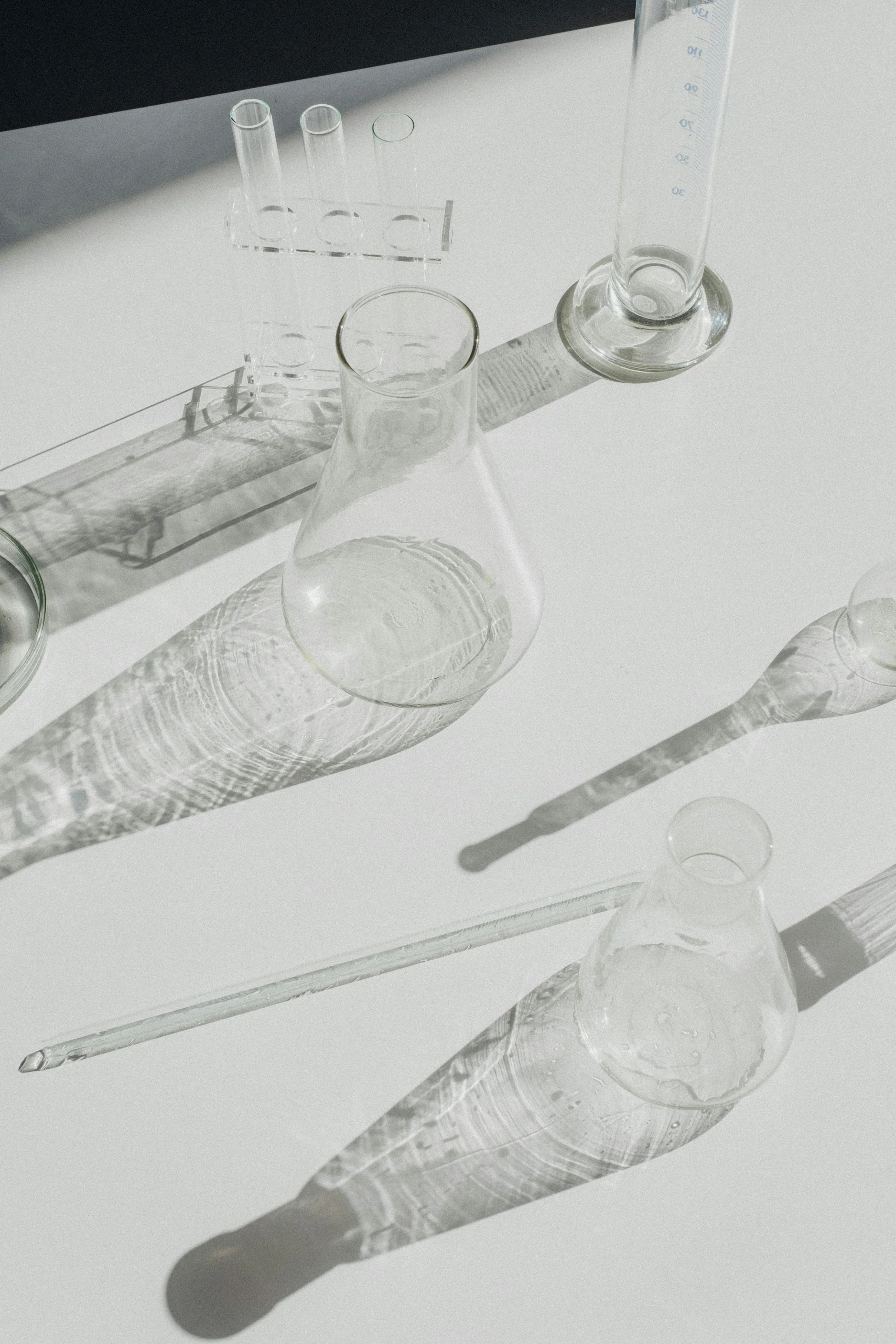 Laboratory glassware on white surface with shadows and reflections.