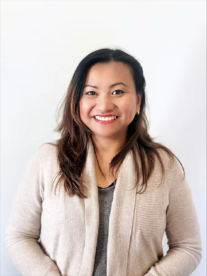 A woman with long dark hair smiling, wearing a beige cardigan over a gray top, against a plain white background.