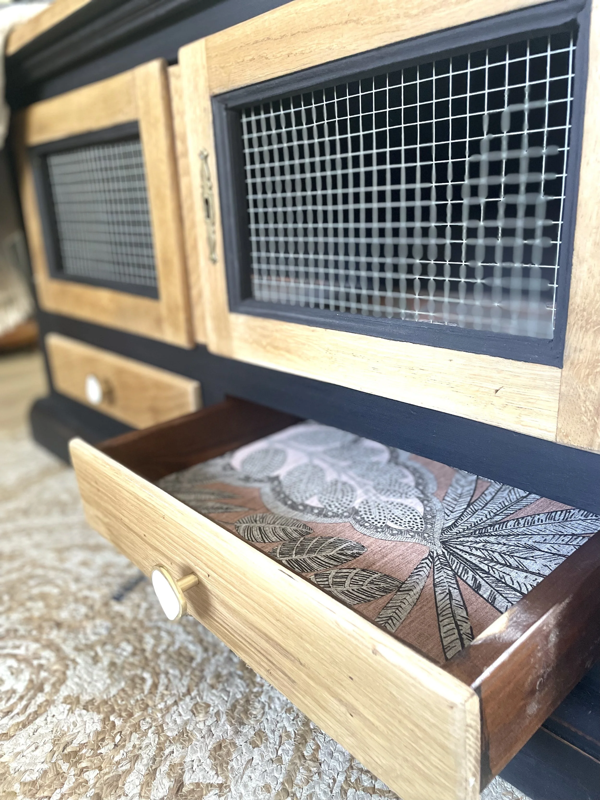 Une étagère en bois avec des porte-mousquets en grillage. Une tiroir en bois avec un motif de feuilles dessinées à l'intérieur.