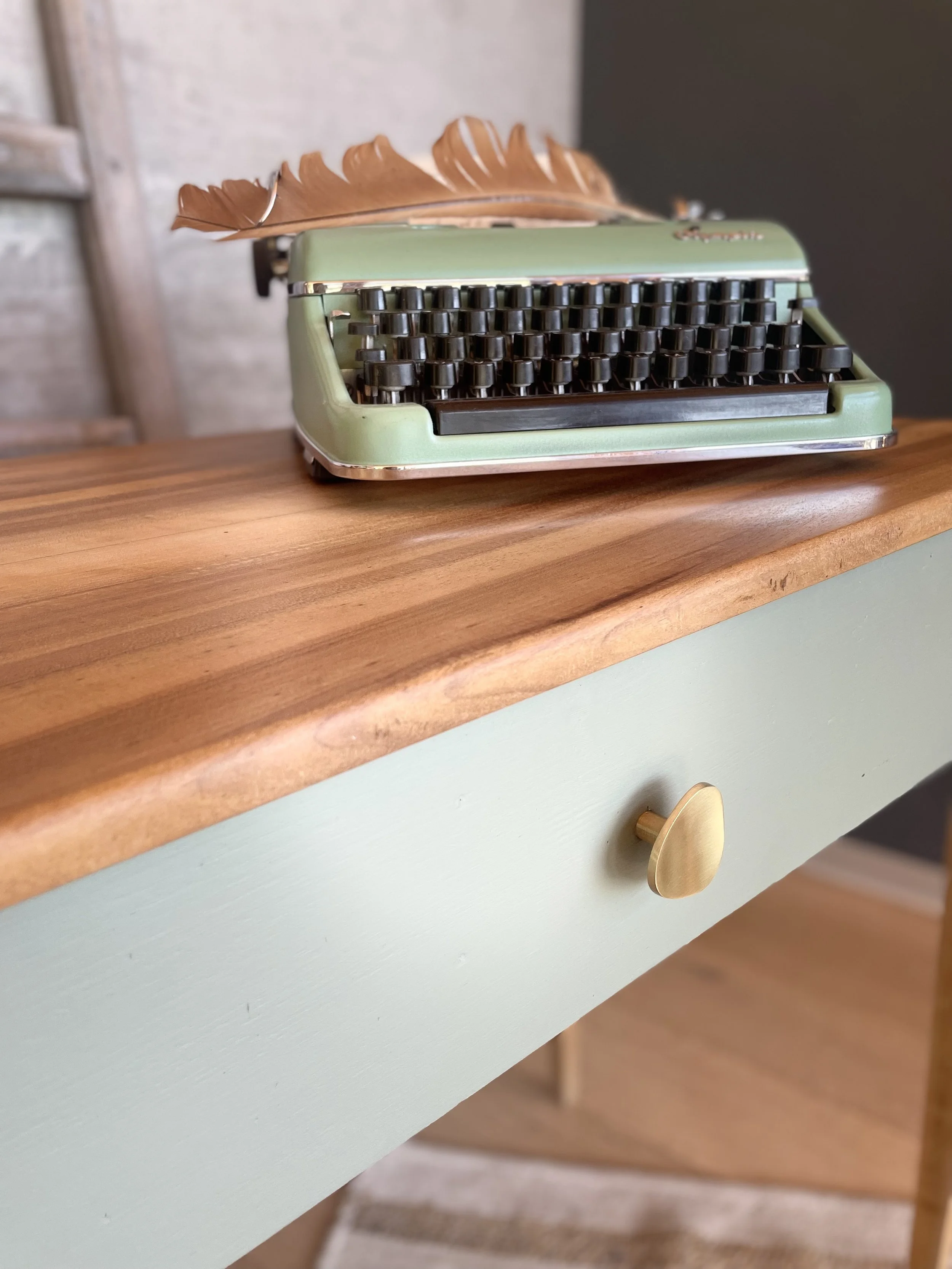 Une machine à écrire vintage verte avec une plume en bois posée dessus, placée sur une table en bois.