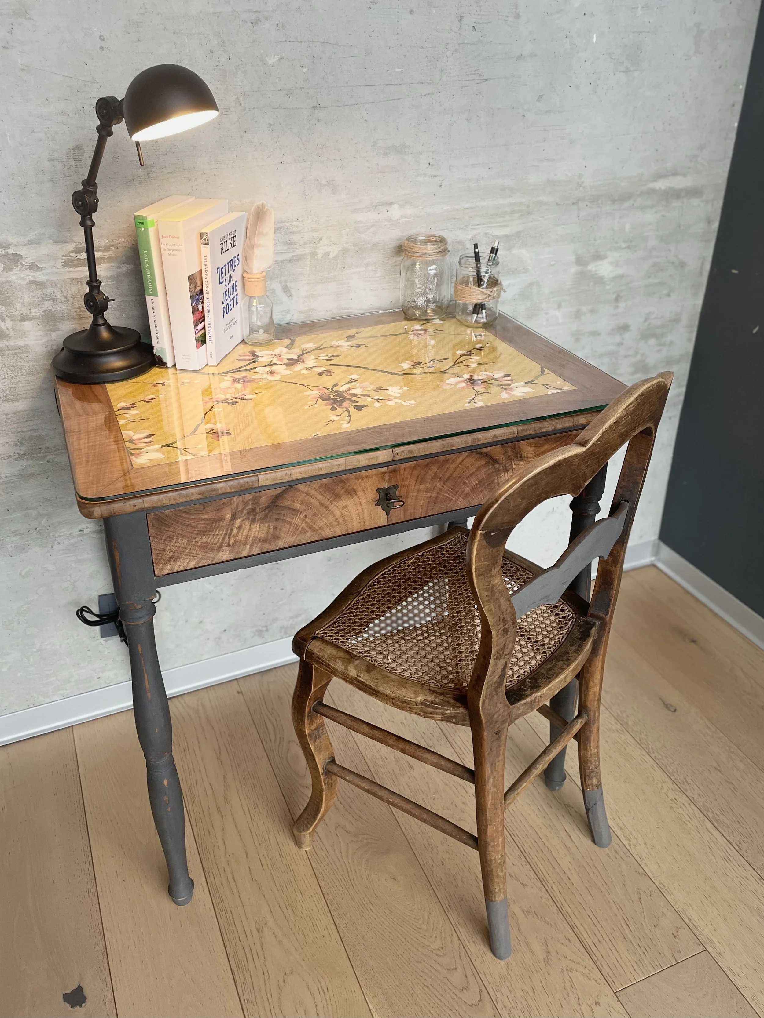 Bureau en bois avec surface en verre et chaise ancienne en bois, lampe de bureau allumée, livres, pots en verre avec fournitures de bureau sur le bureau.