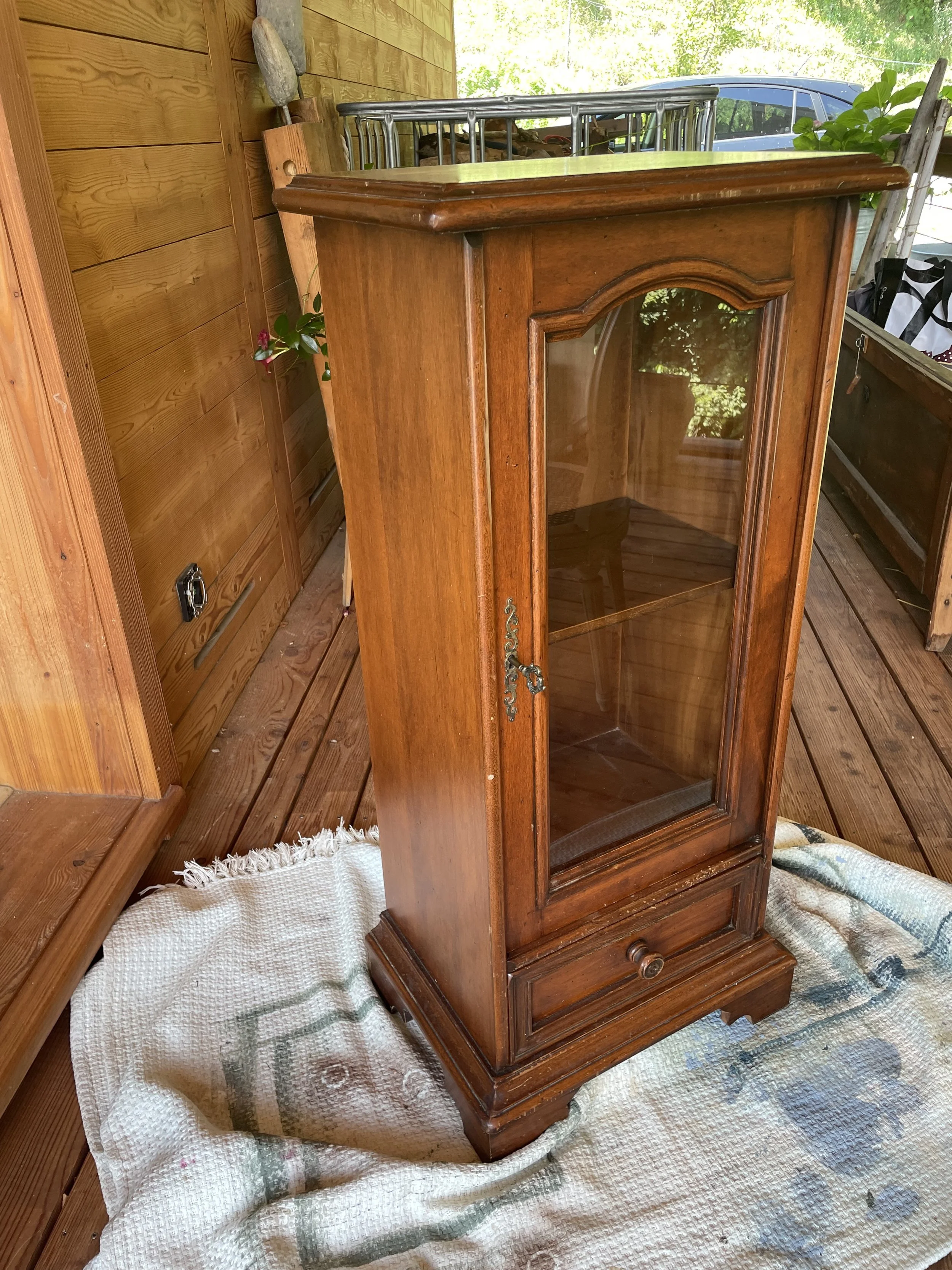 Une vitrine en bois avec une porte en verre, située sur une terrasse en bois.