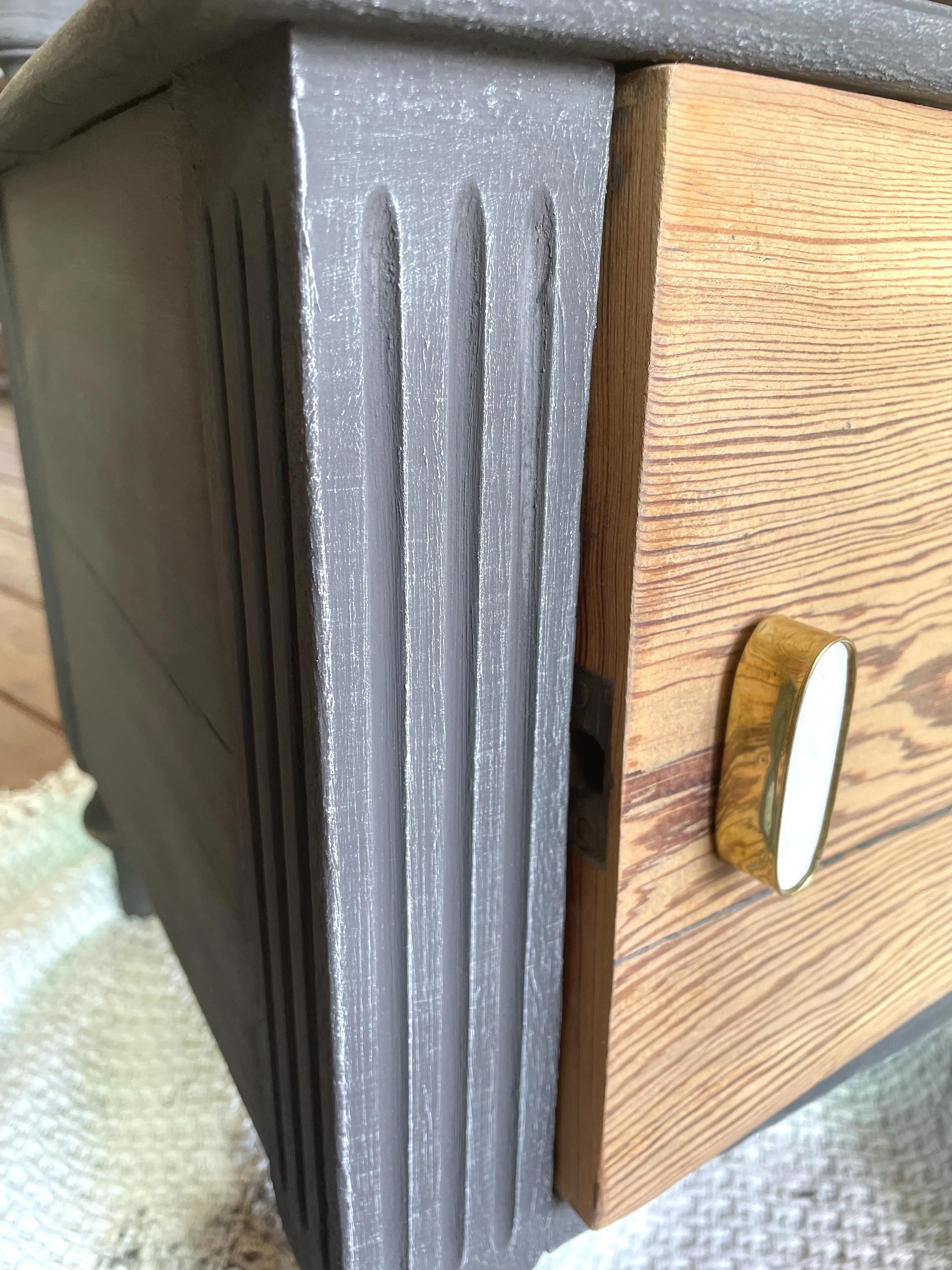 Gros plan d'un meuble en bois avec un bouton doré, associé à un cadre gris avec des rainures verticales, vu de côté