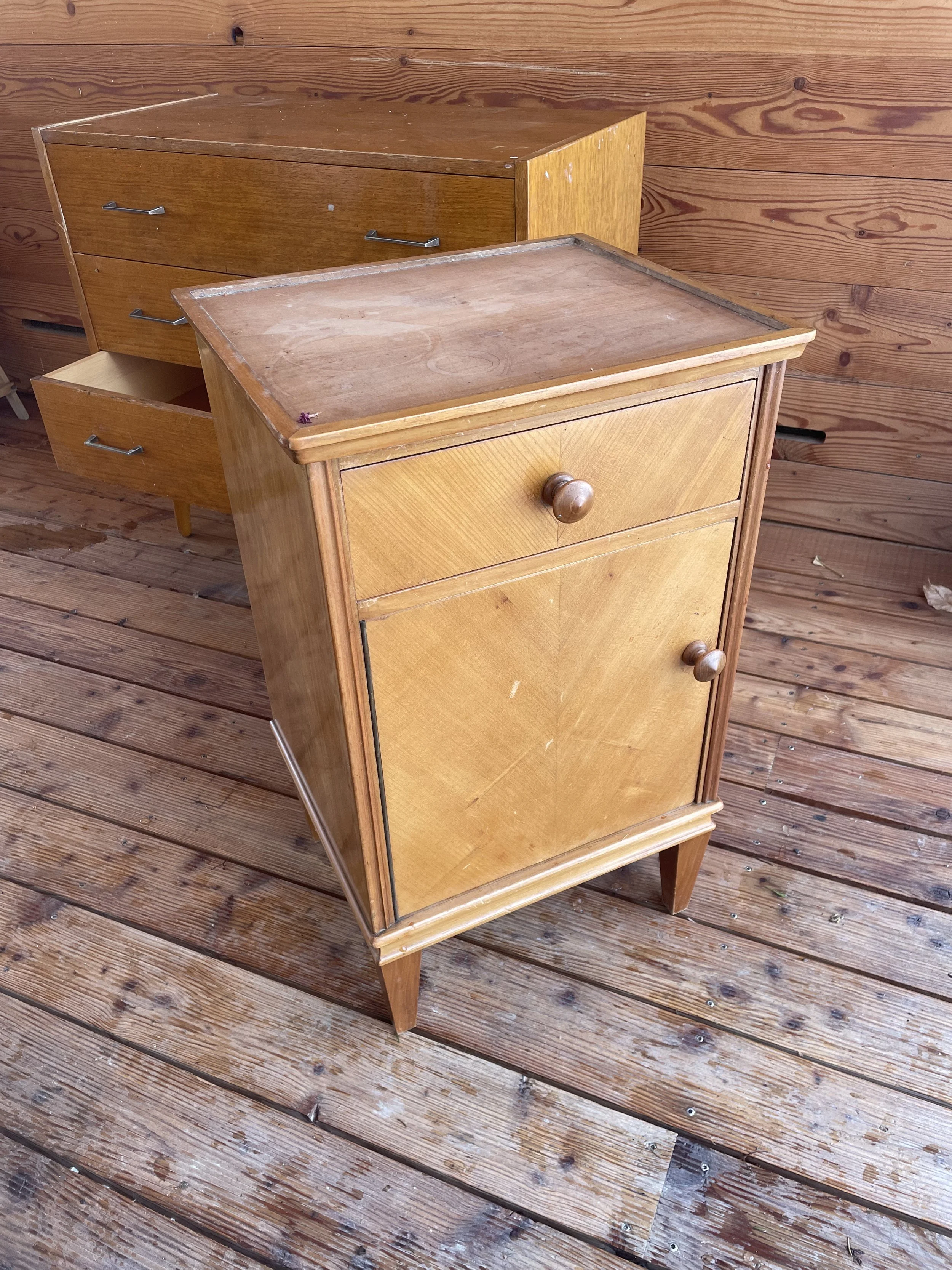 Petite armoire en bois avec une porte à un seul tiroir en haut, située sur un sol en bois avec un fond en bois également.